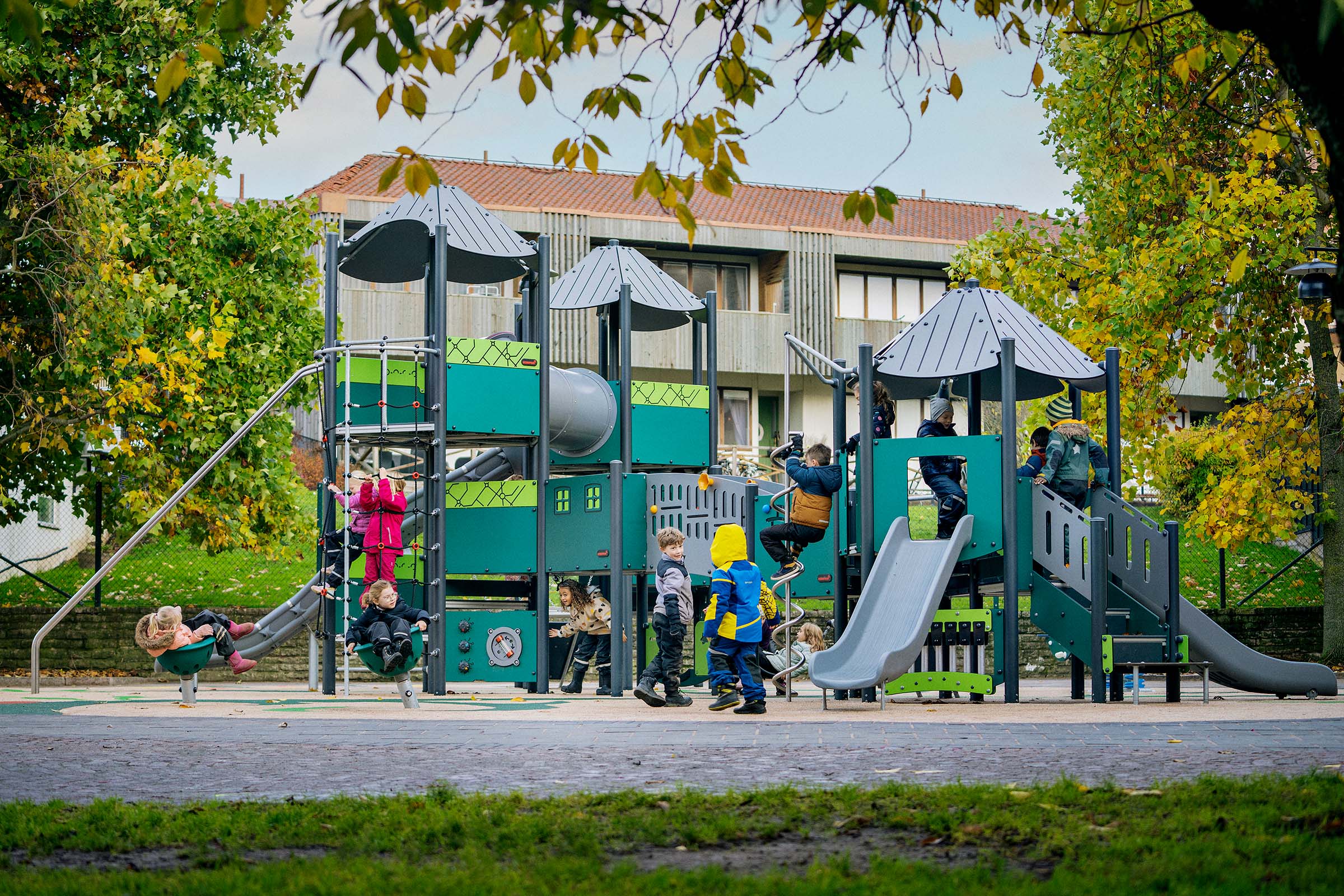 Viele Kinder spielen fröhlich auf einem Spielplatz mit Klettergerüst und freistehenden Spielgeräten