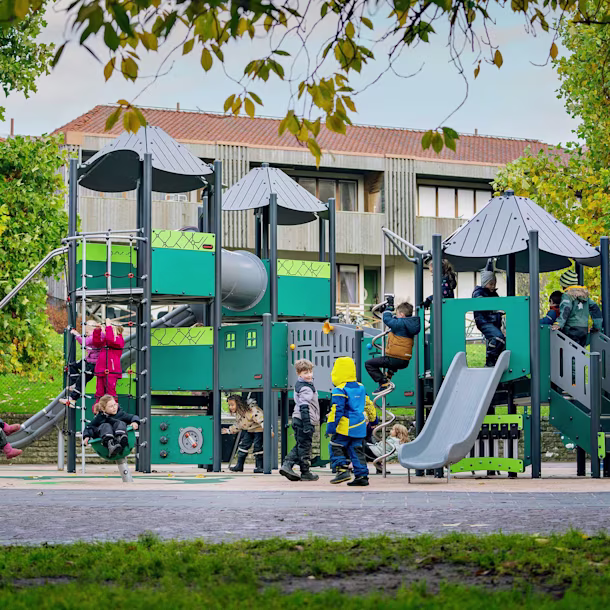 Viele Kinder spielen fröhlich auf einem Spielplatz mit Klettergerüst und freistehenden Spielgeräten