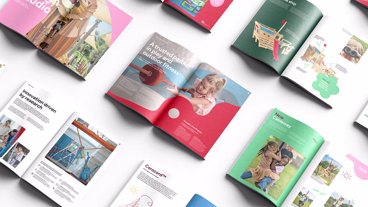 Colorful open brochures on a white surface showing playground equipment, children playing, and design studio layouts.