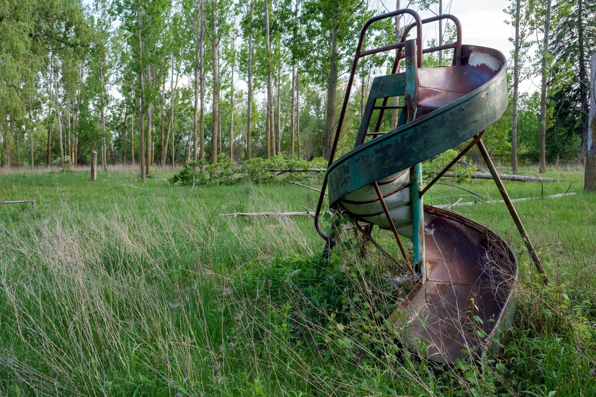 a rusty slide in the middle of a grassy field.
