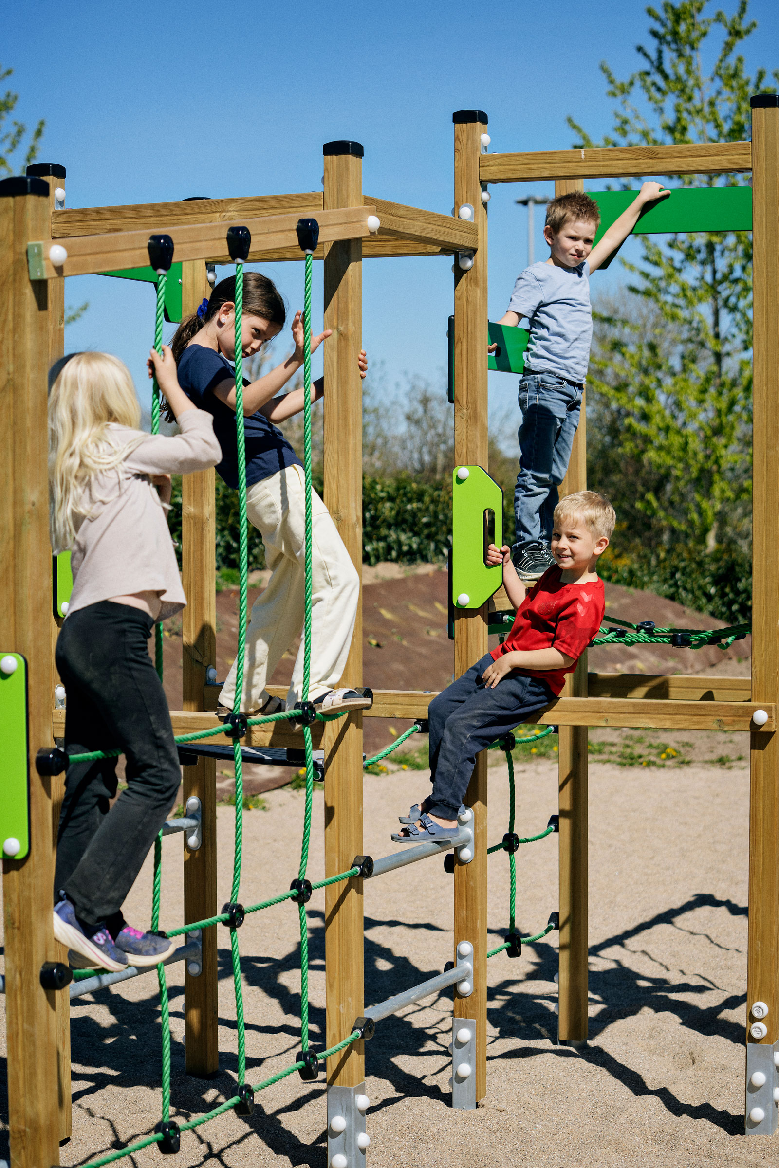 Children climbing and hanging on a wooden and green playground structure on a sunny day with blue sky and clouds