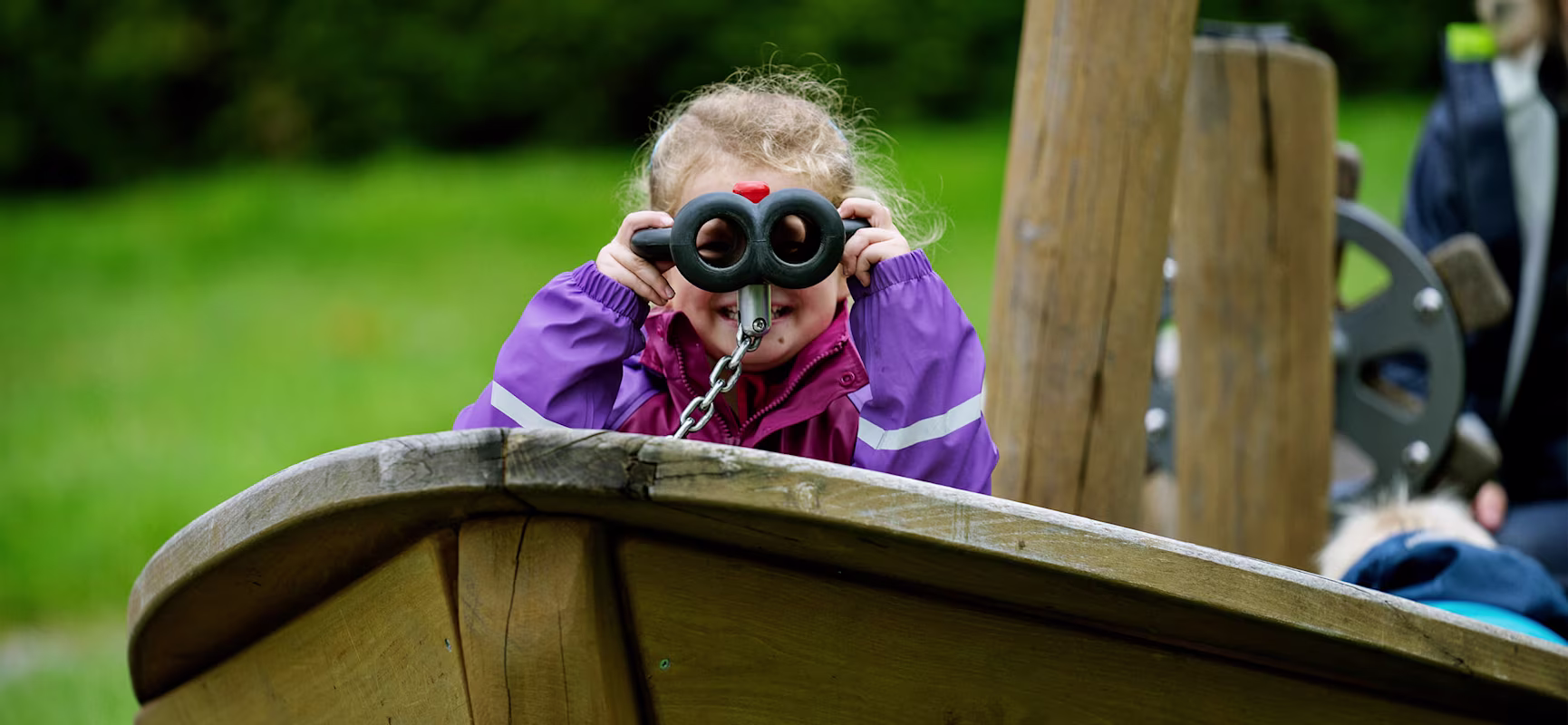 Pre-school girl looking through binoculars in a wooden playground boat
