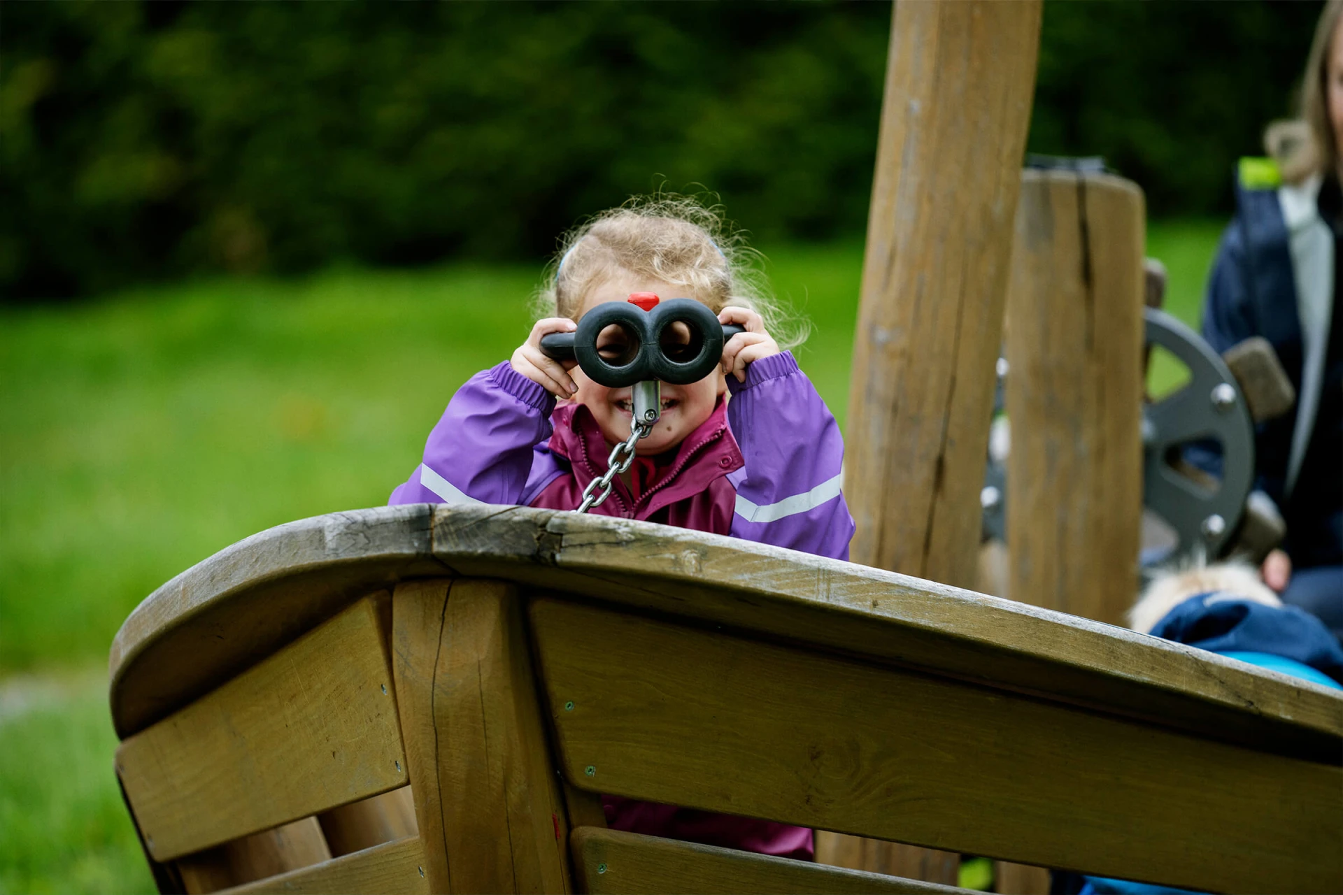 Pre-school girl looking through binoculars in a wooden playground boat