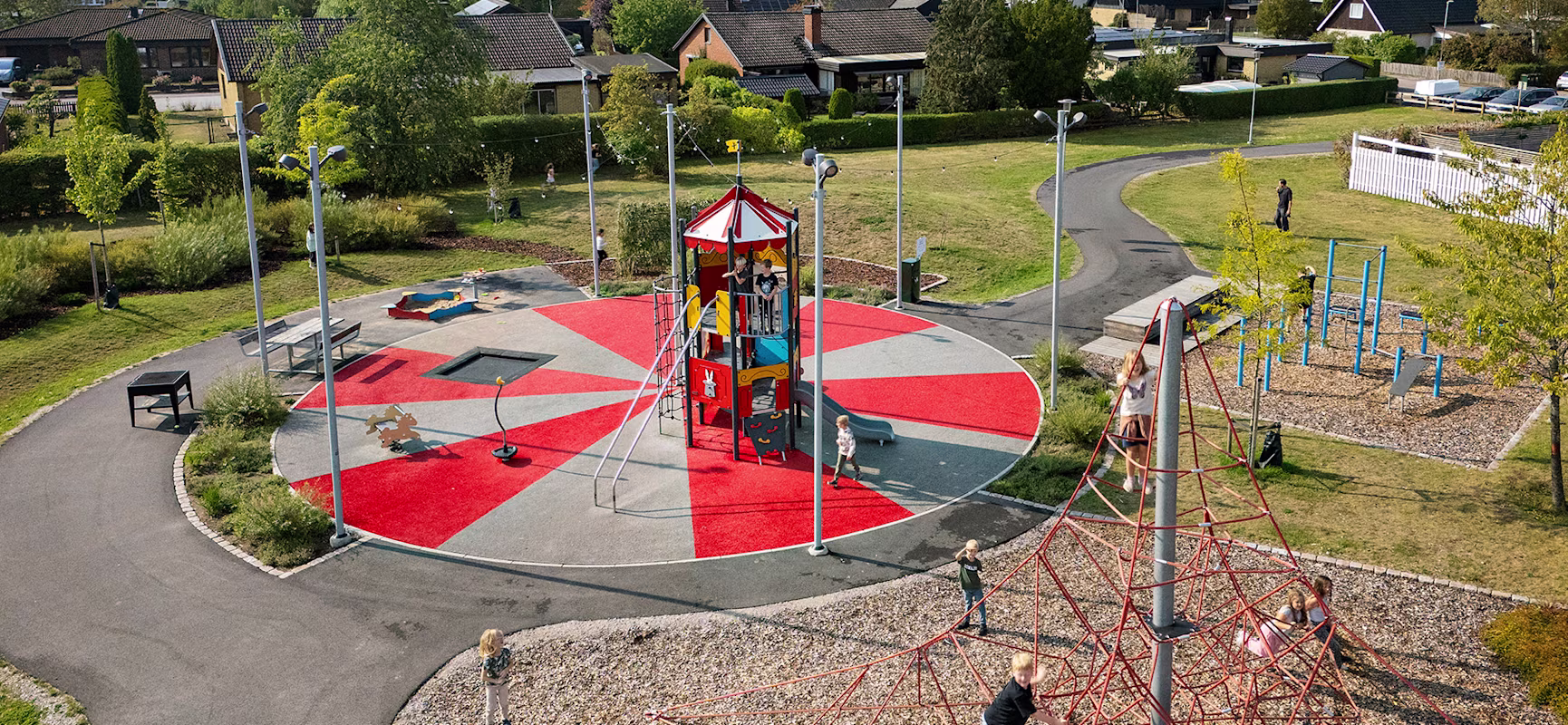 Barn som leker på en lekplats med cirkustema med utegym i bakgrunden