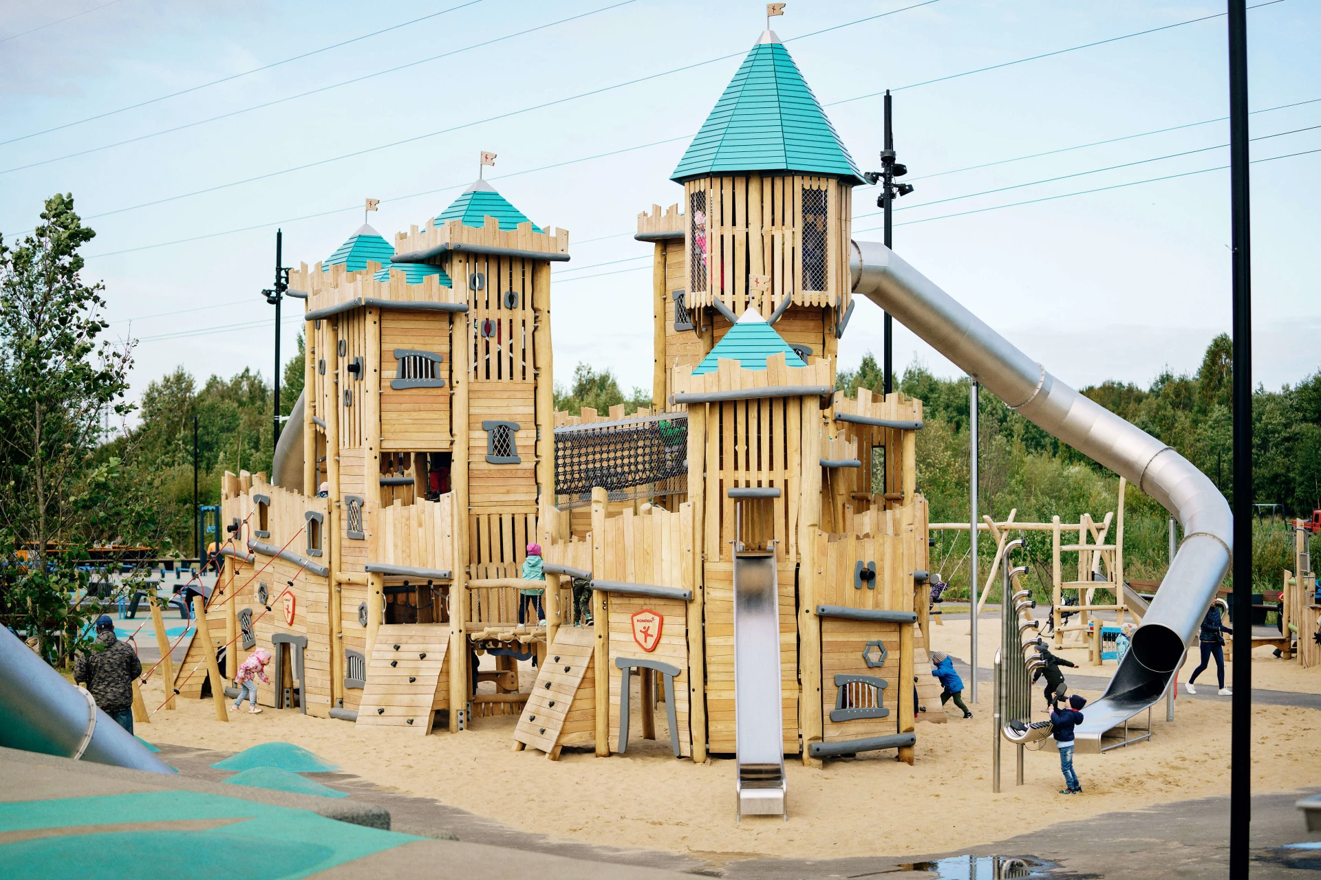 Large wooden playground castle sitting on top of sand surfacing. The castle has a large metal tunnel slide going from the top to the bottom. Showstopping pieces like this one are ideal for playground projects at zoos and other leisure facilities.