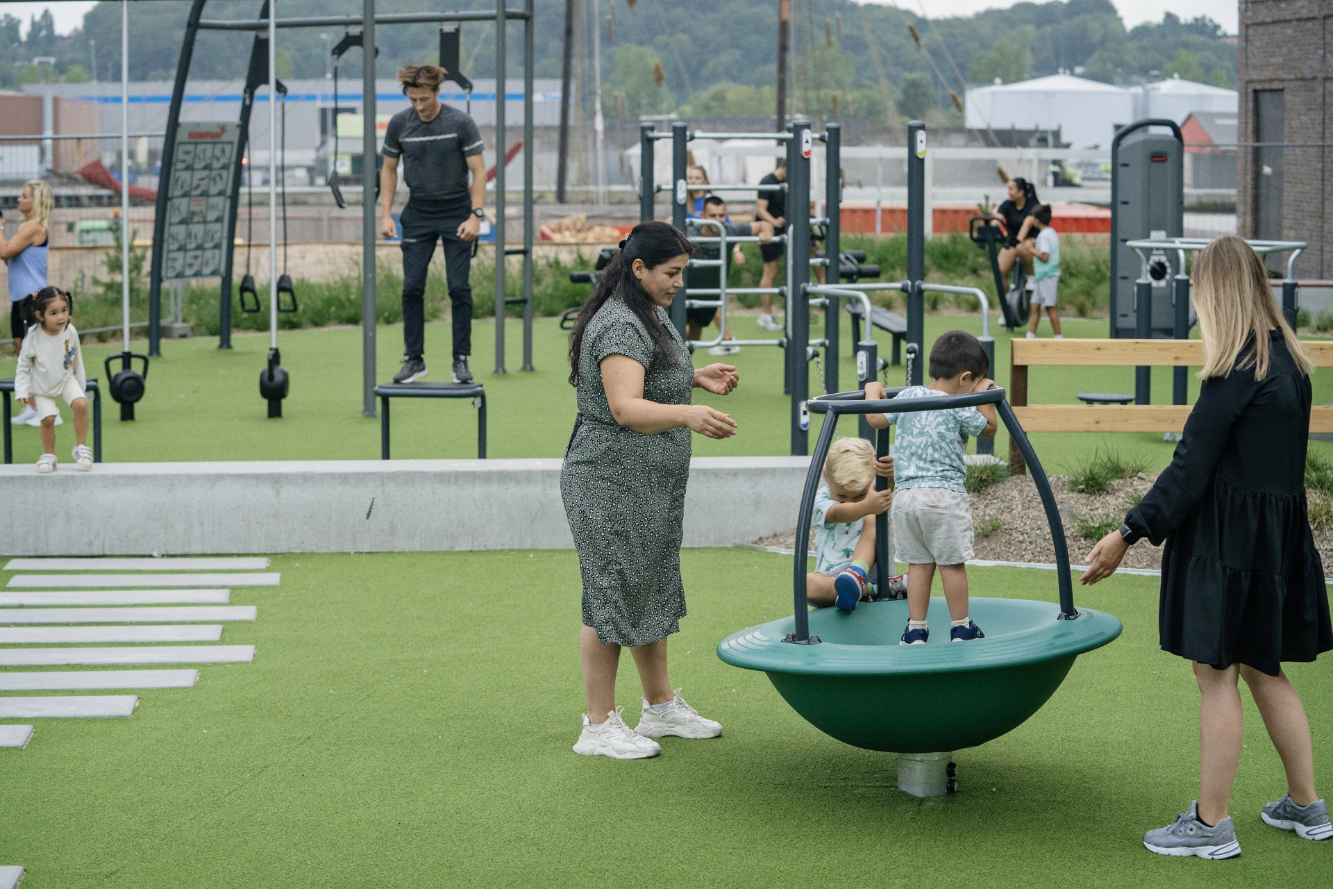 Barn leker på en lekplats medan vuxna tränar i ett utegym