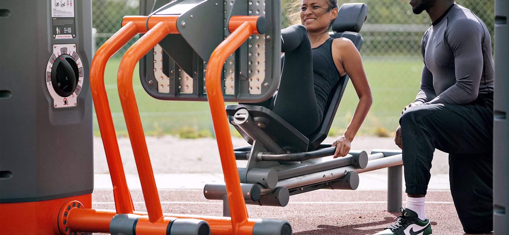 A man and a woman working out outdoors on KOMPAN fitness equipment.
