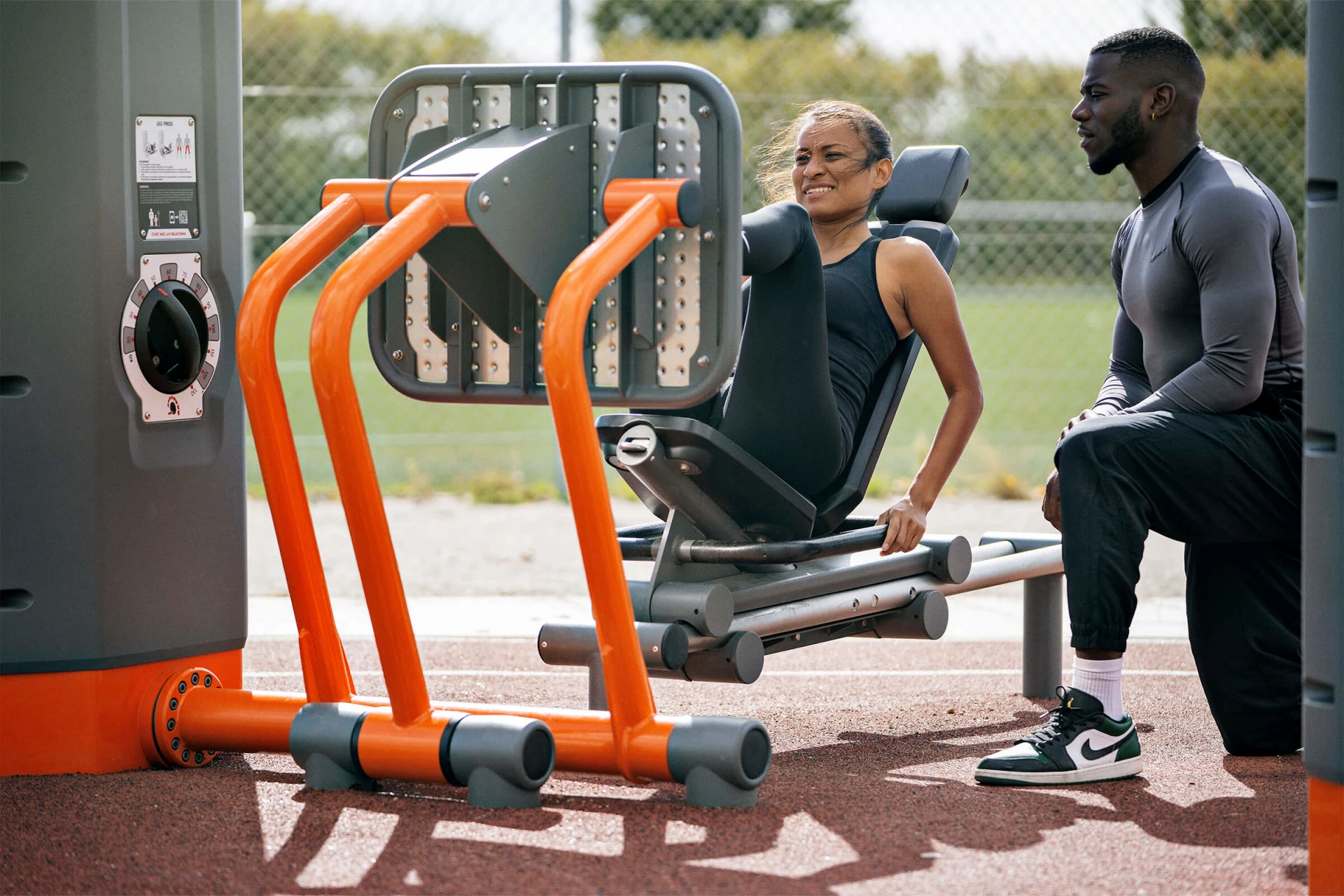 A man and a woman working out outdoors on KOMPAN fitness equipment. 
