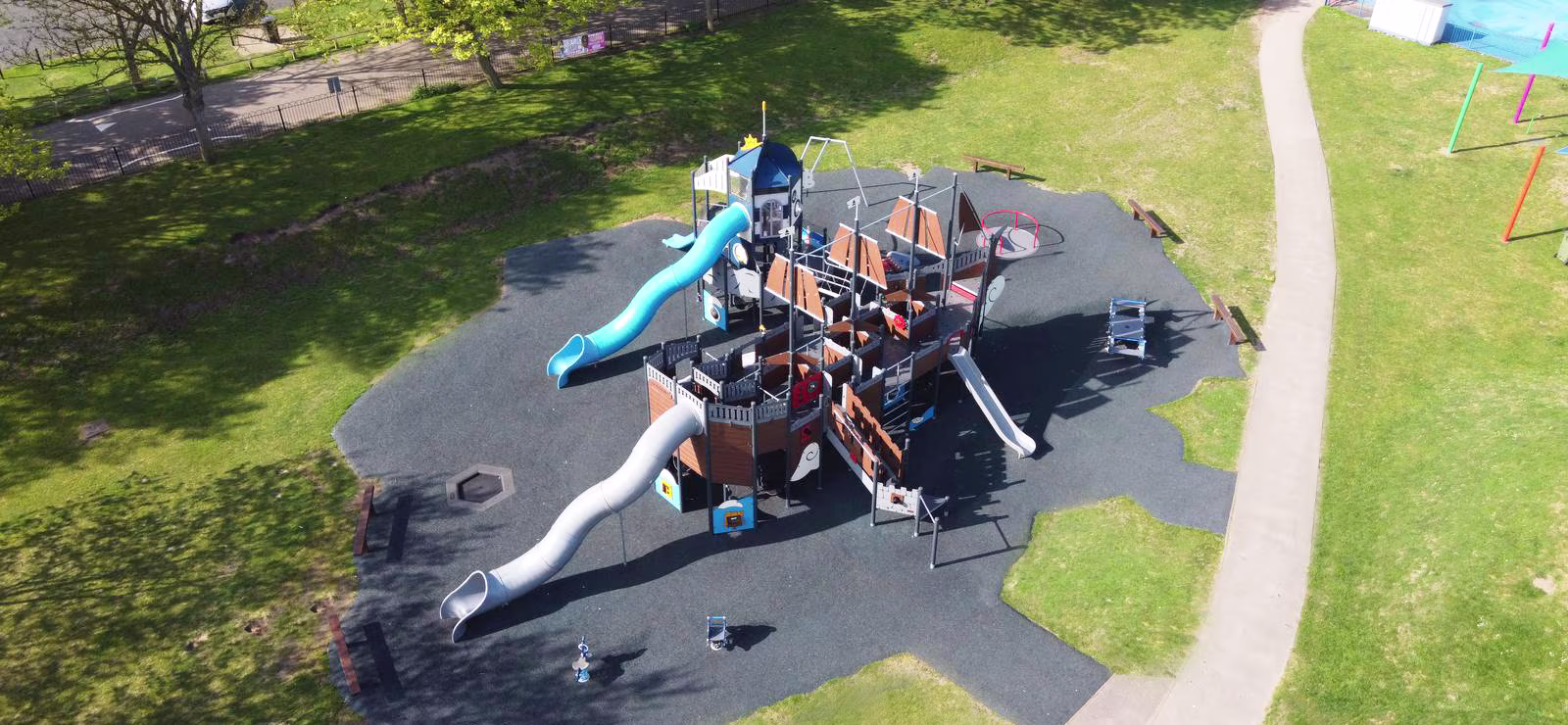 Aerial view of a large pirate ship playground with slides and climbing frames on soft flooring, surrounded by grass and paths