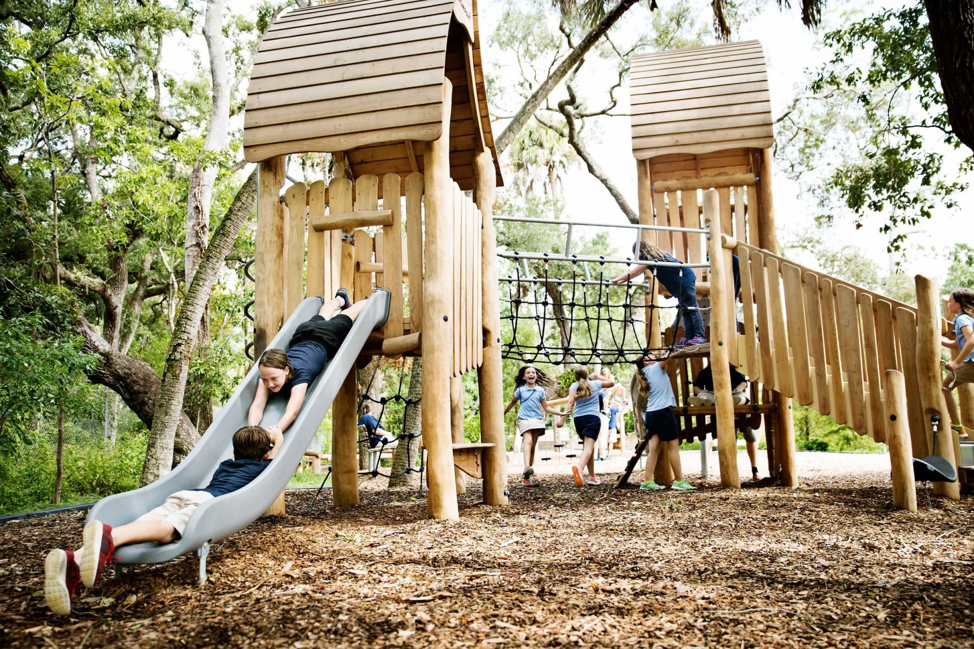 children playing on a large natural playground play huts made from robinia wood