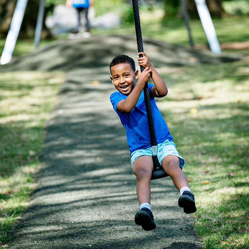 spielender und lachender Junge auf einer Spielplatz Seilbahn in einem öffentlichen Park 
