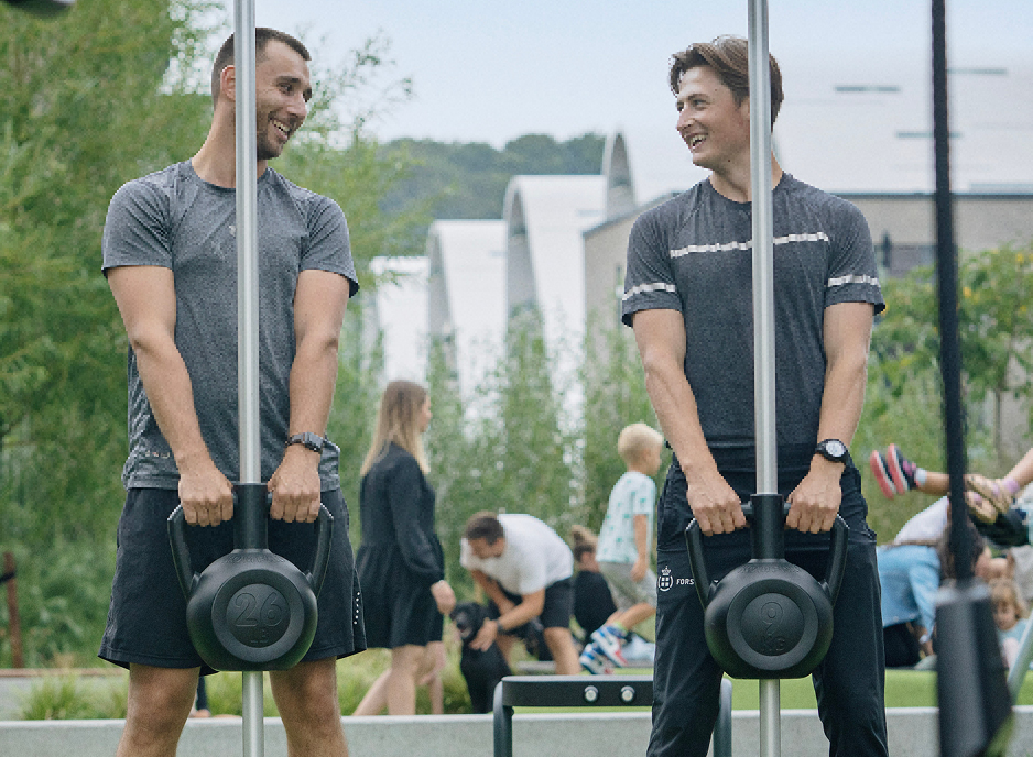 Two men standing next to each other holding kettlebells.