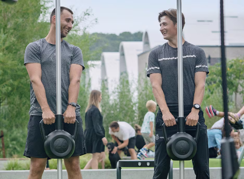 Two men standing next to each other holding kettlebells.