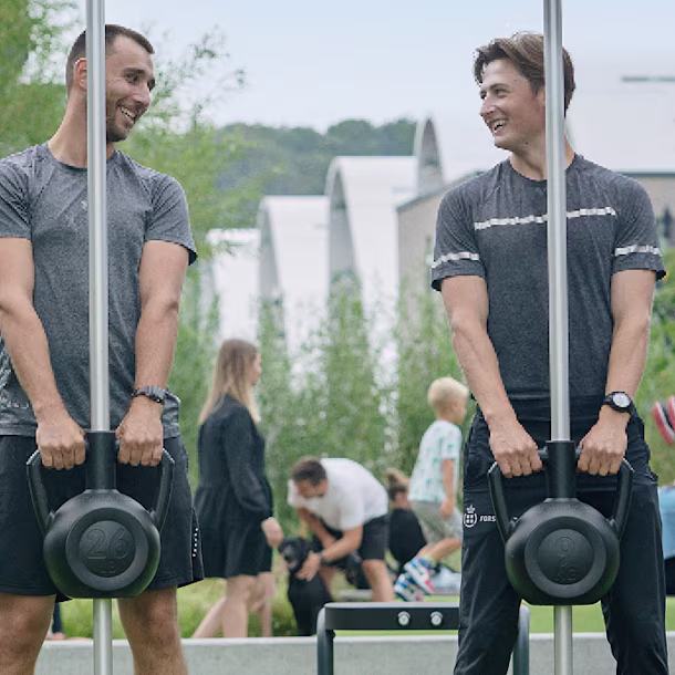 Two men standing next to each other holding kettlebells.