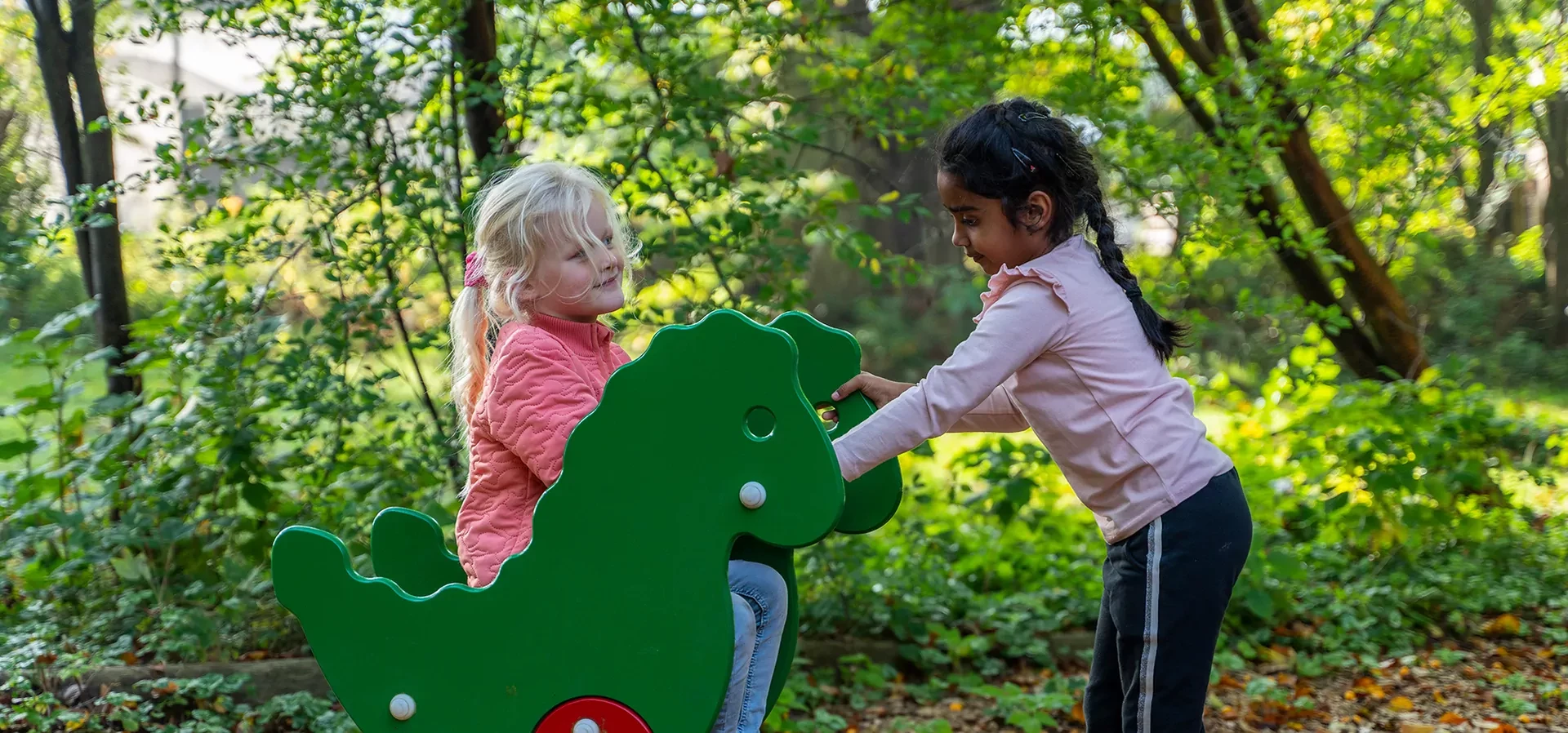 tytöt leikkimässä dinosauruksen muotoisella jousikeinulla leikkipuistossa pääkuva