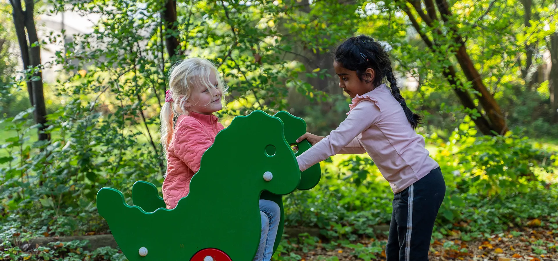 Zwei Mädchen, die auf einem Spielplatz an dem Drachen-Federwippe spielen