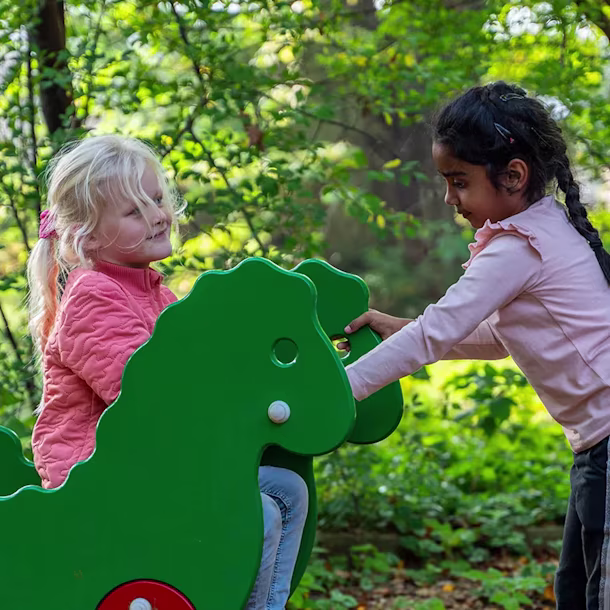 Zwei Mädchen, die auf einem Spielplatz an dem Drachen-Federwippe spielen