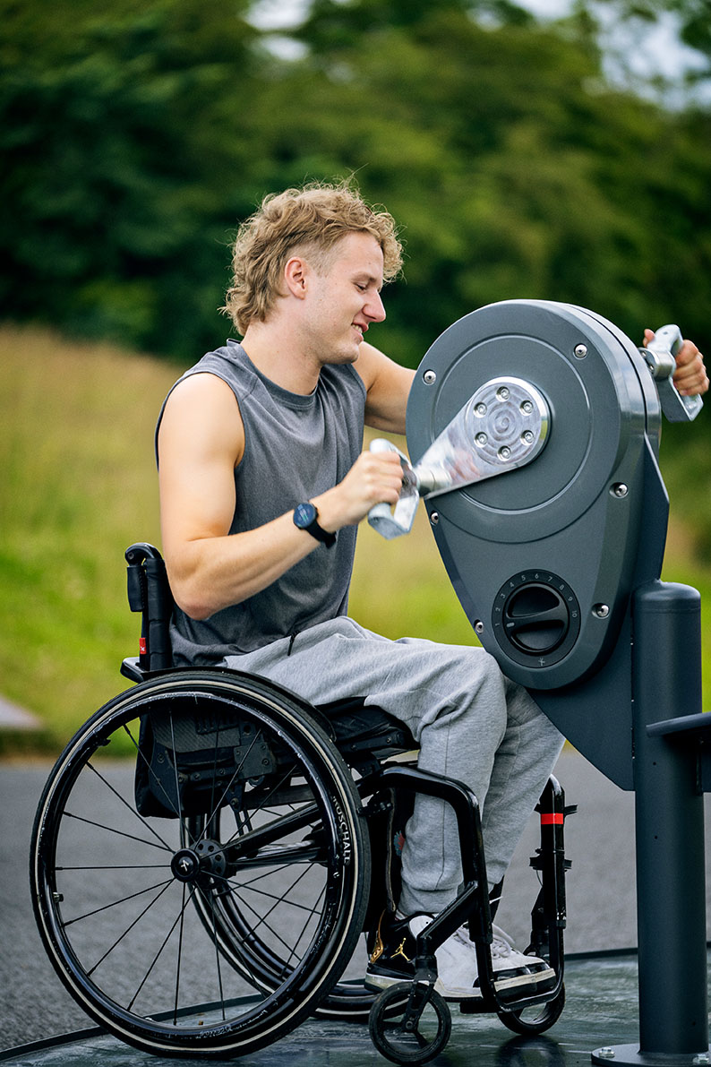Male in a wheelchair using KOMPAN outdoor fitness arm bike