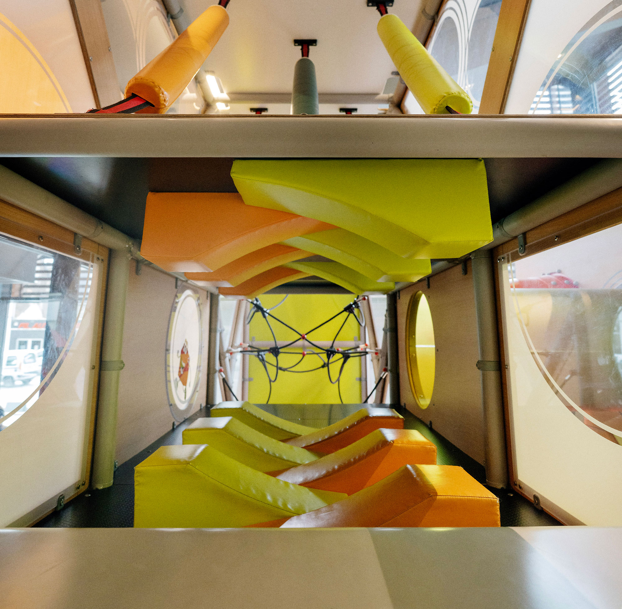 Interior of a bright indoor play tunnel with yellow and orange foam obstacles and climbing ropes at the far end