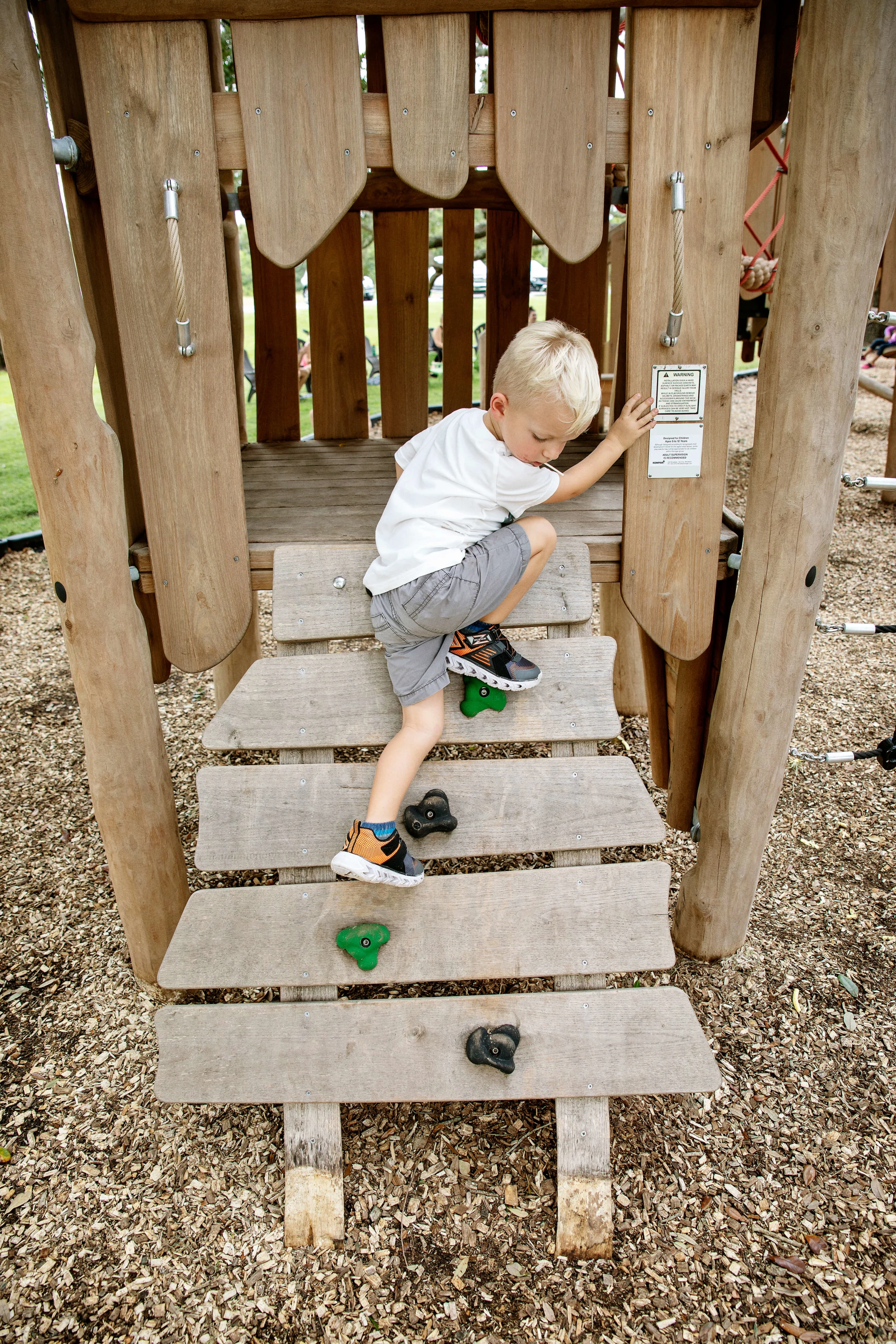 A young boy climbing on wooden play equipment. The floor below is natural coloured bark chippings. The aesthetic of your playground construction project can change the purpose and overall result. Be sure to choose wisely!