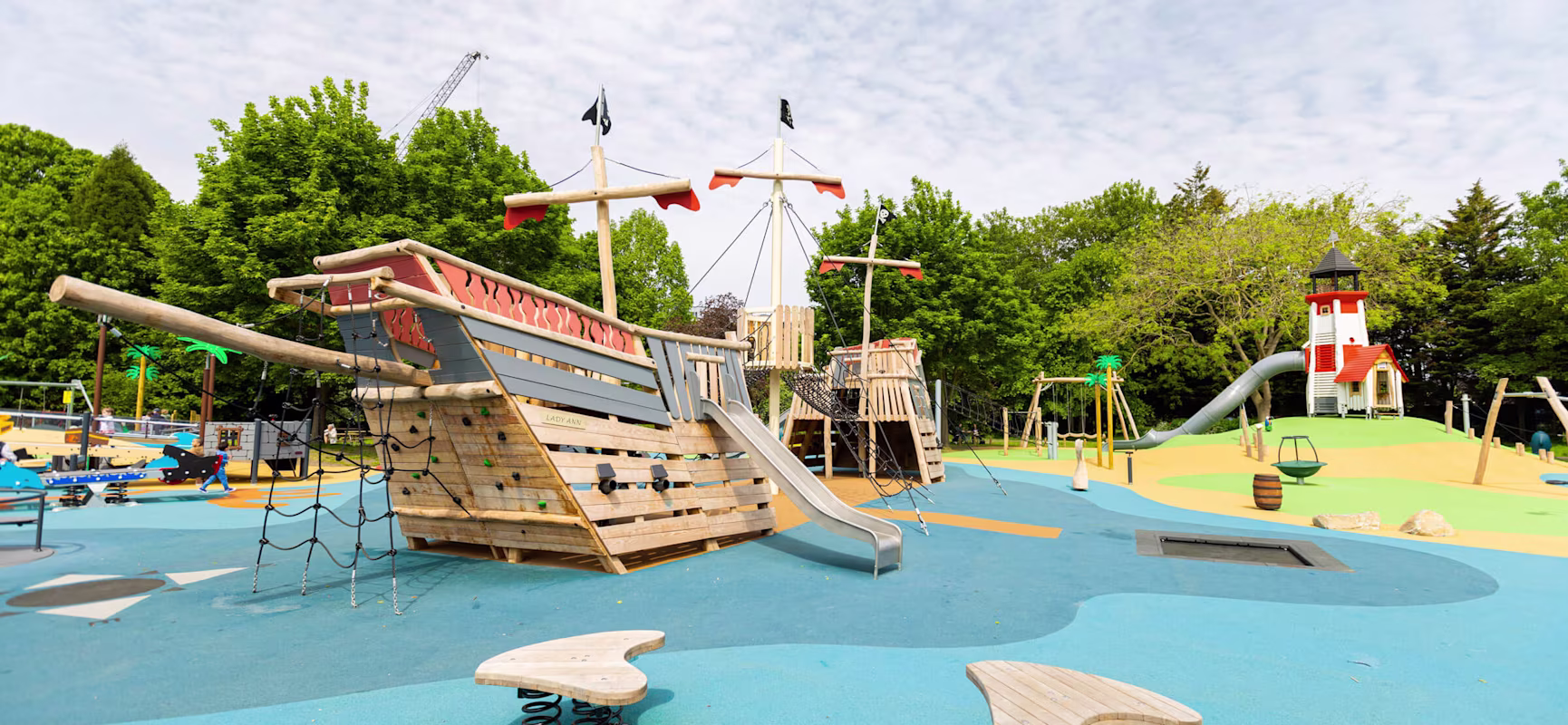 a playground with a wooden pirate ship and lighthouse playground sculpture