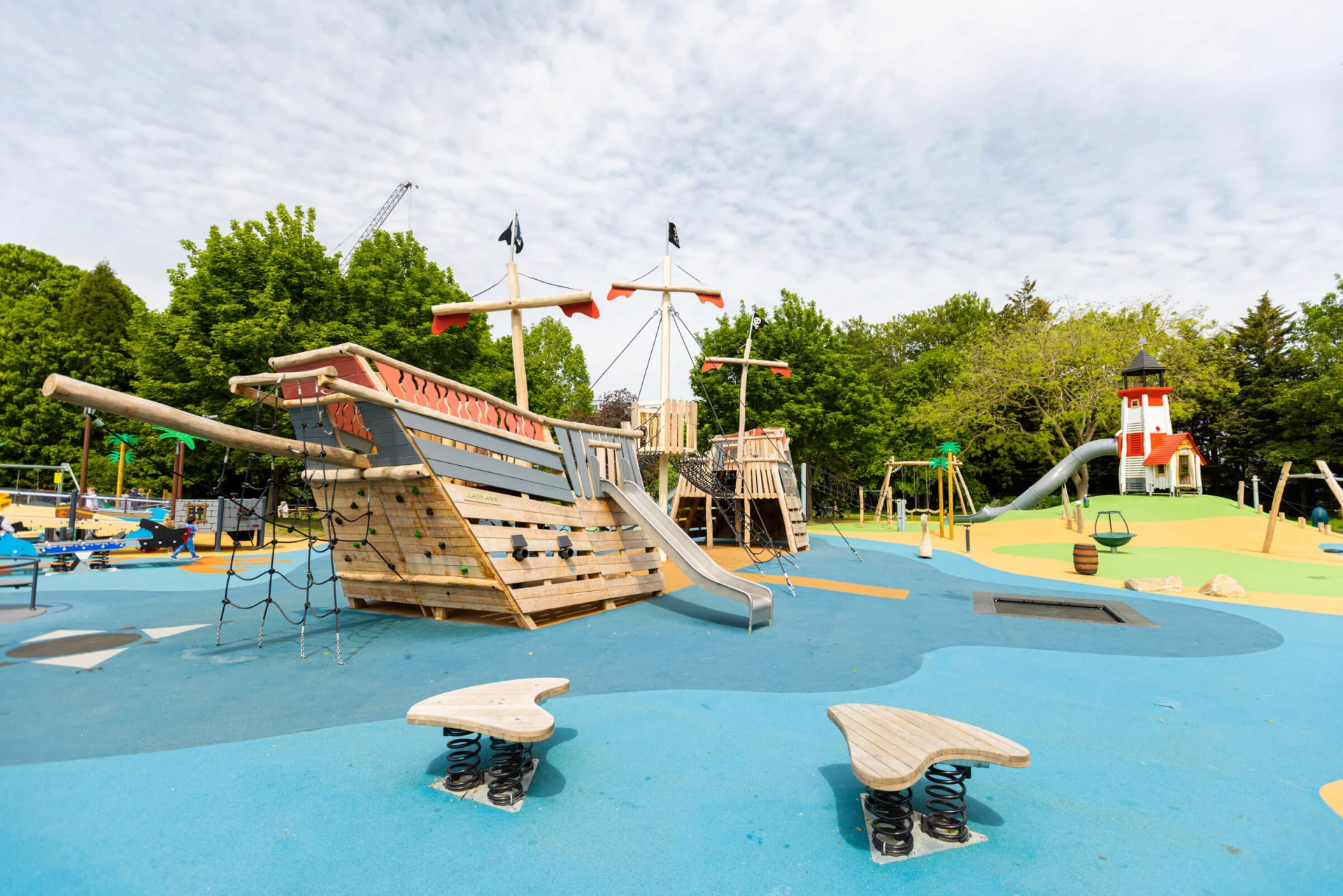 a playground with a wooden pirate ship and lighthouse playground sculpture