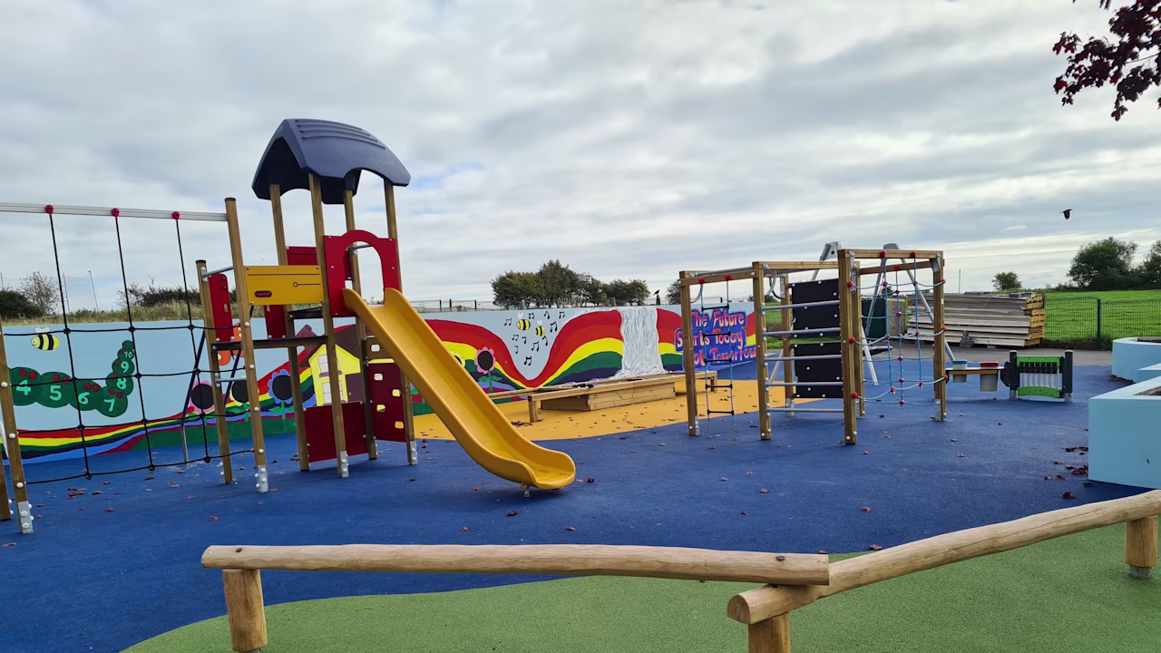 Children playing on a colourful, tree-themed playground with slides, climbing frames and numbered leaf markings in a city courtyard