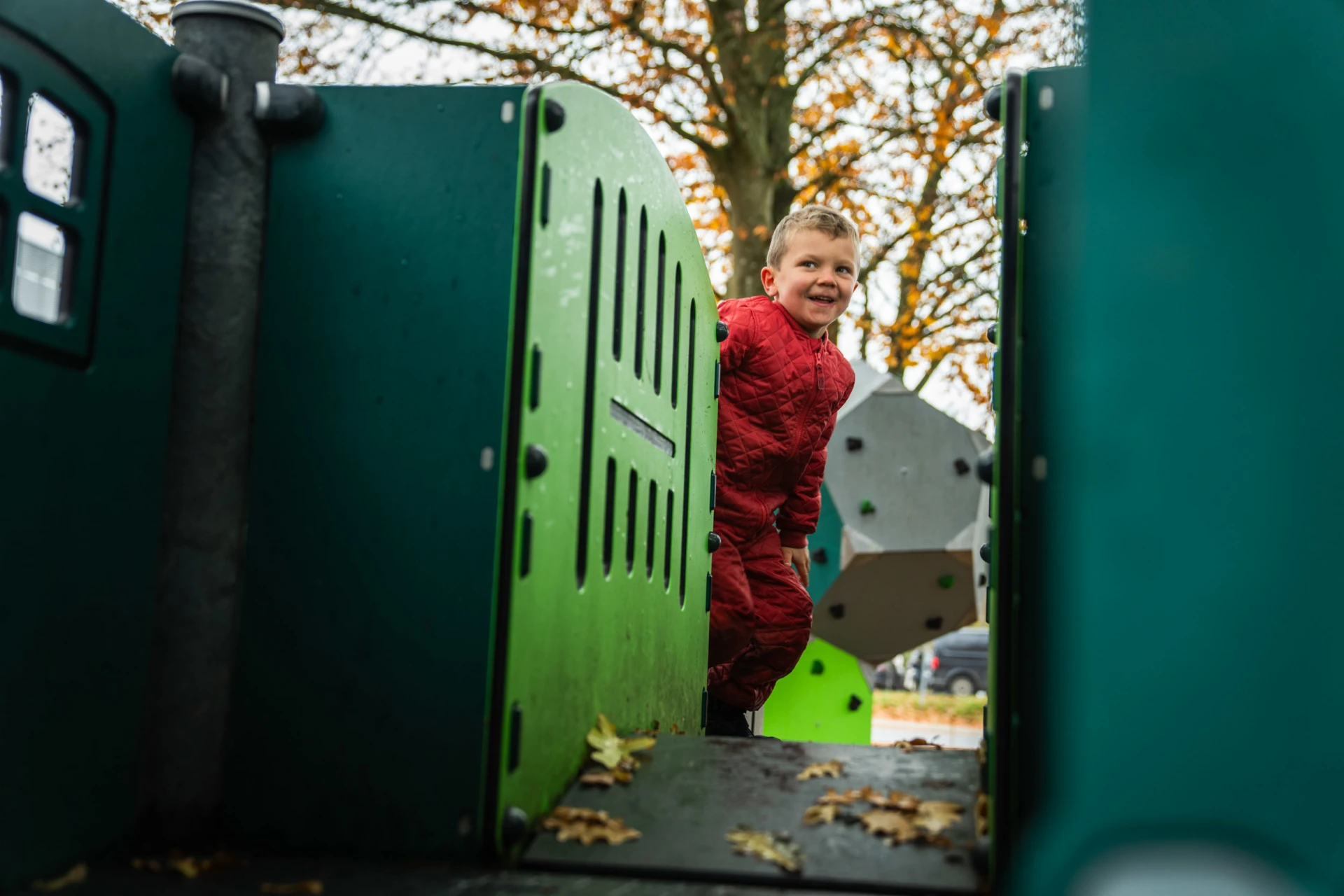 Bambino vestito di rosso che gioca su una struttura verde del parco giochi