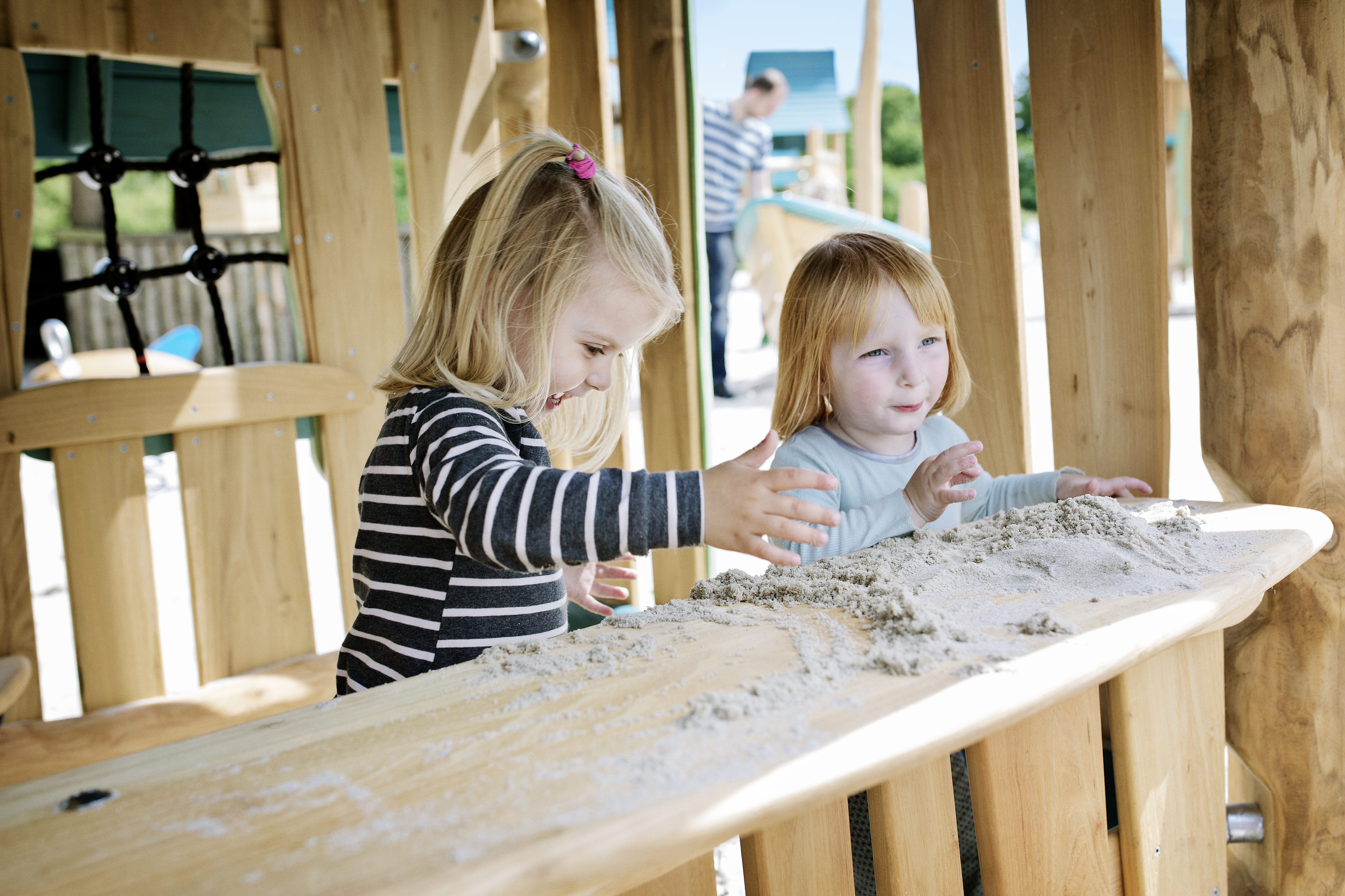 two small girls playing with sand at a wooden playhouse in Givskud Zoo