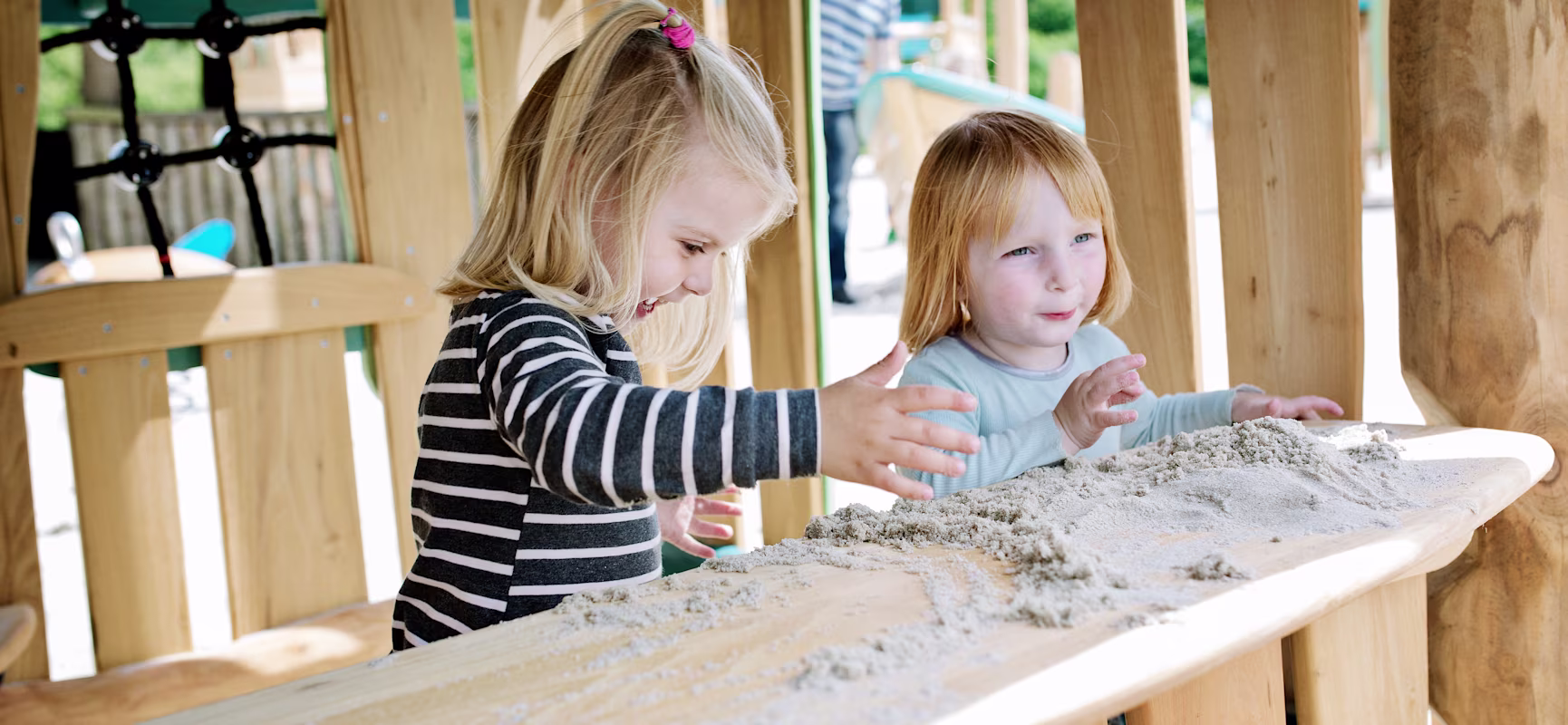 two small girls playing with sand at a wooden playhouse in Givskud Zoo