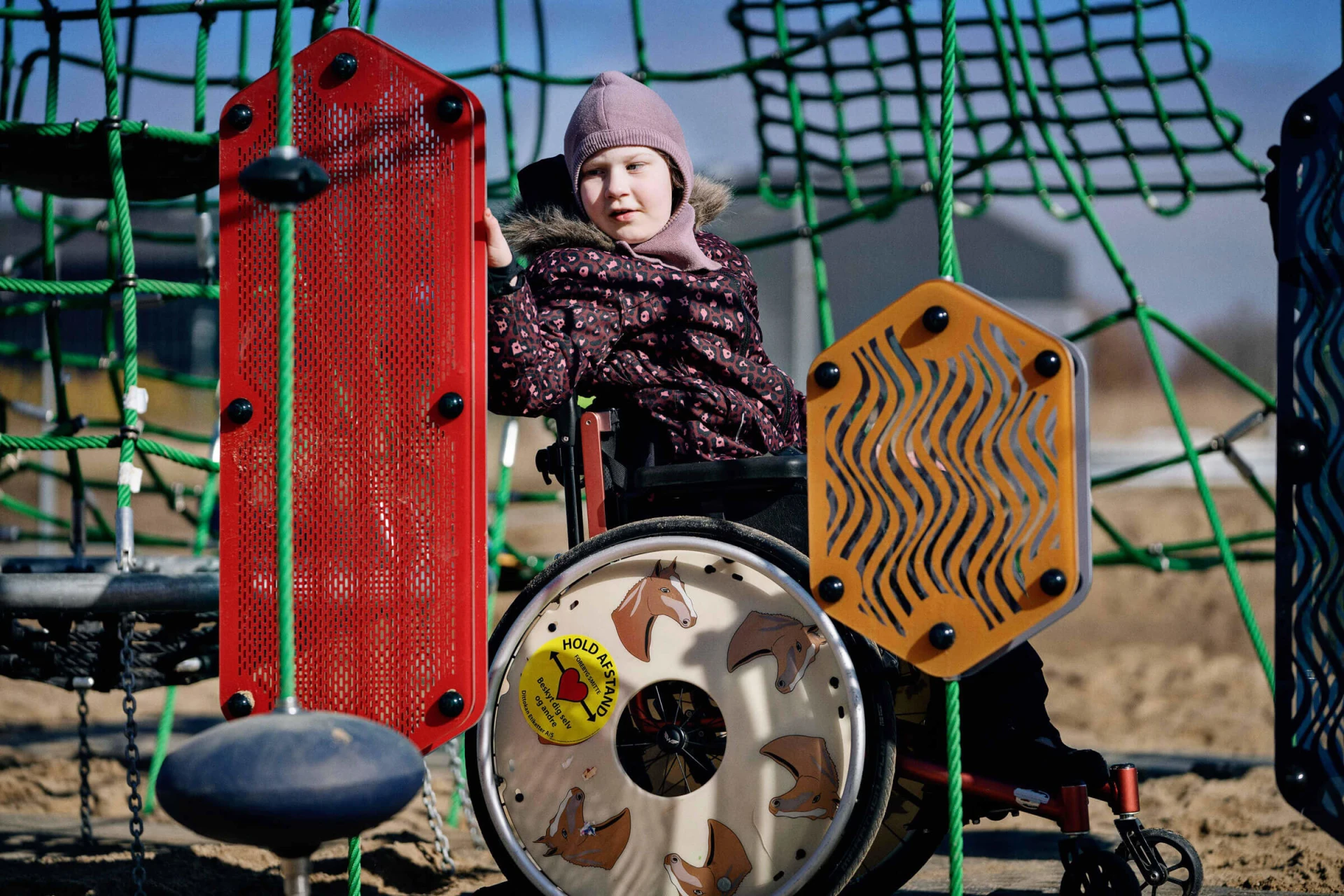 pyörätuolia käyttävä tyttö leikkimässä aistileikkipaneeleilla leikkipuistossa