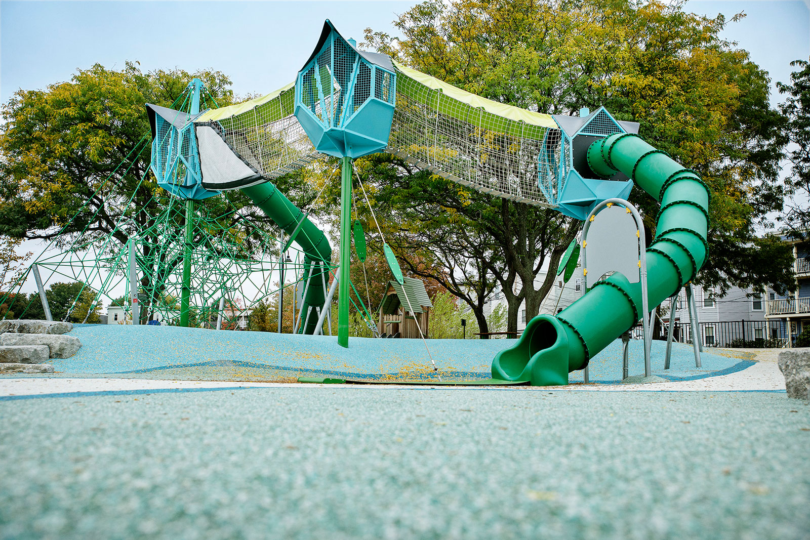 Modern playground with tall green climbing nets, elevated tunnels and twisting tube slides, set among trees on a rubberised surface