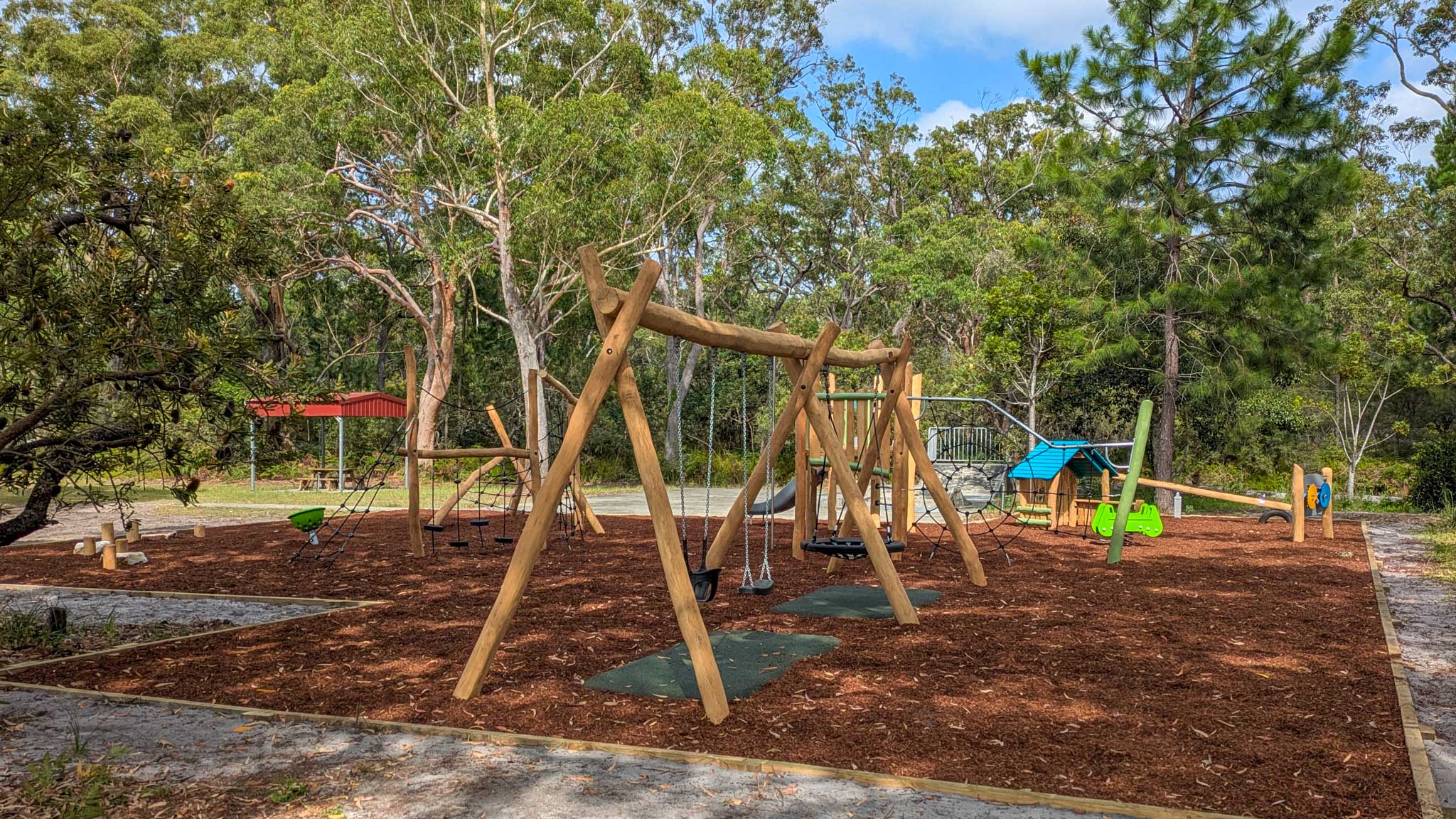 a natural australian playground with wooden outdoor play equipment like swings, climbing equipment, springers, themed play and a slide.