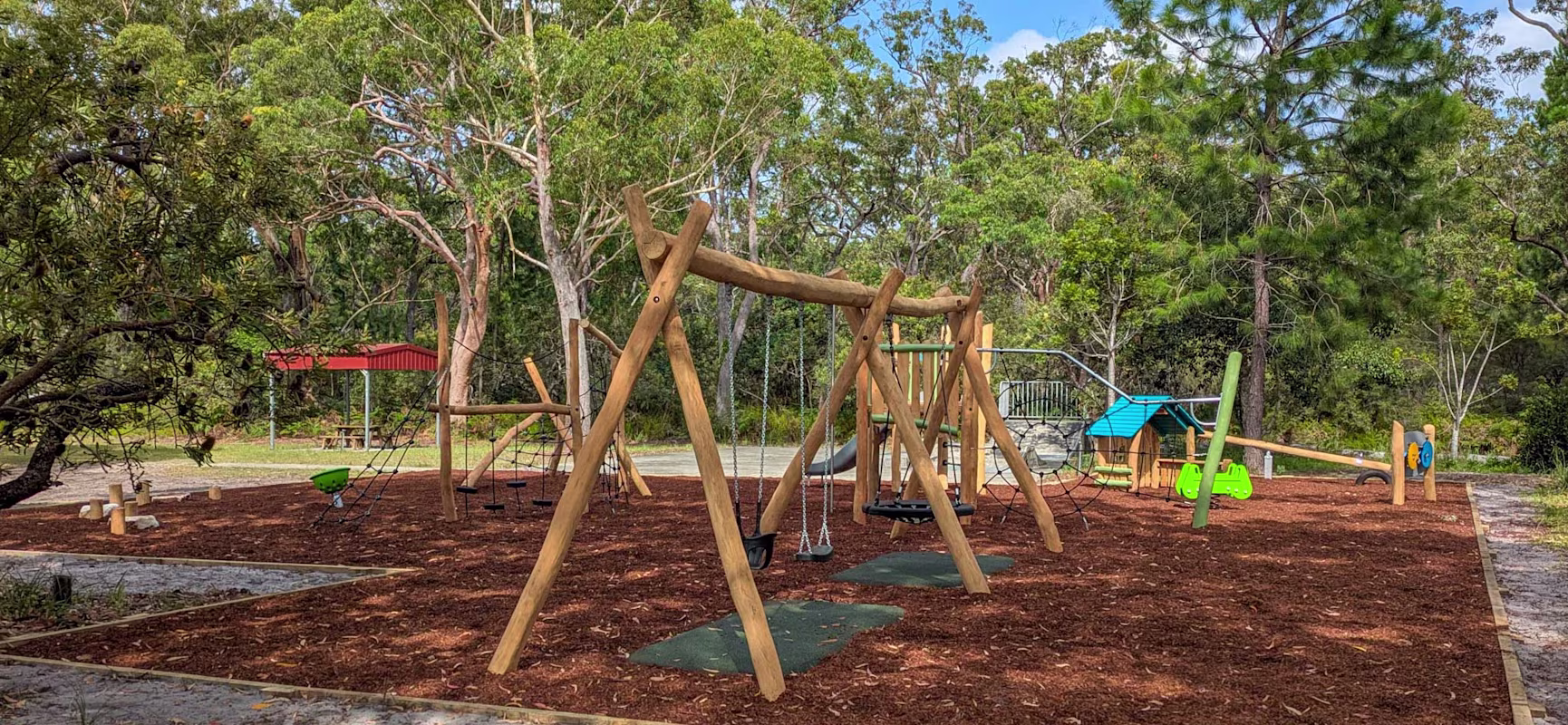 a natural australian playground with wooden outdoor play equipment like swings, climbing equipment, springers, themed play and a slide.