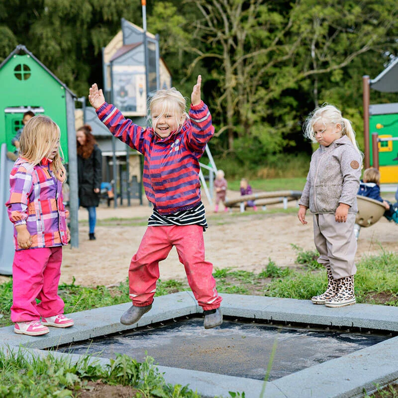 Mädchen hüpft auf Spielplatz Sprungfläche in einem Park 
