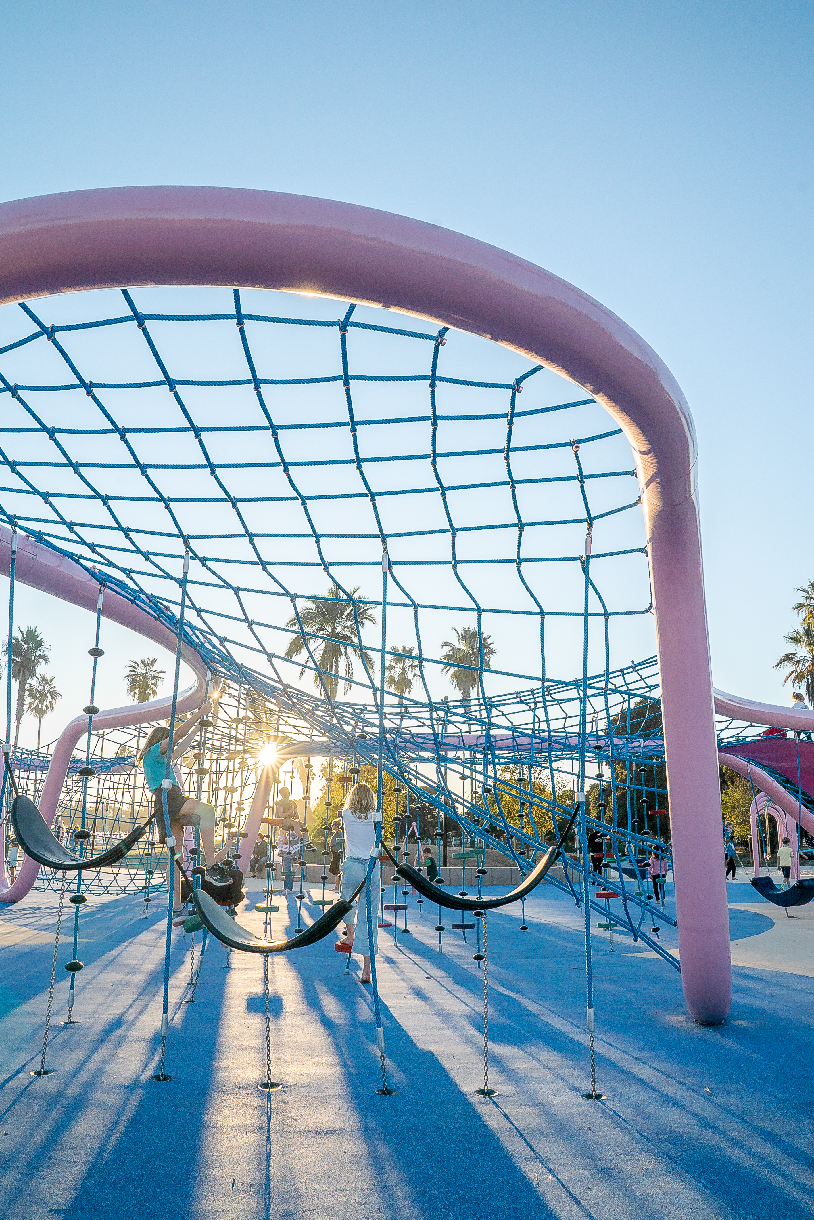 Close-up shot of children playing on a pink rope climbing structure while the sun is going down at Maruta Gardner Park in San Diego, California