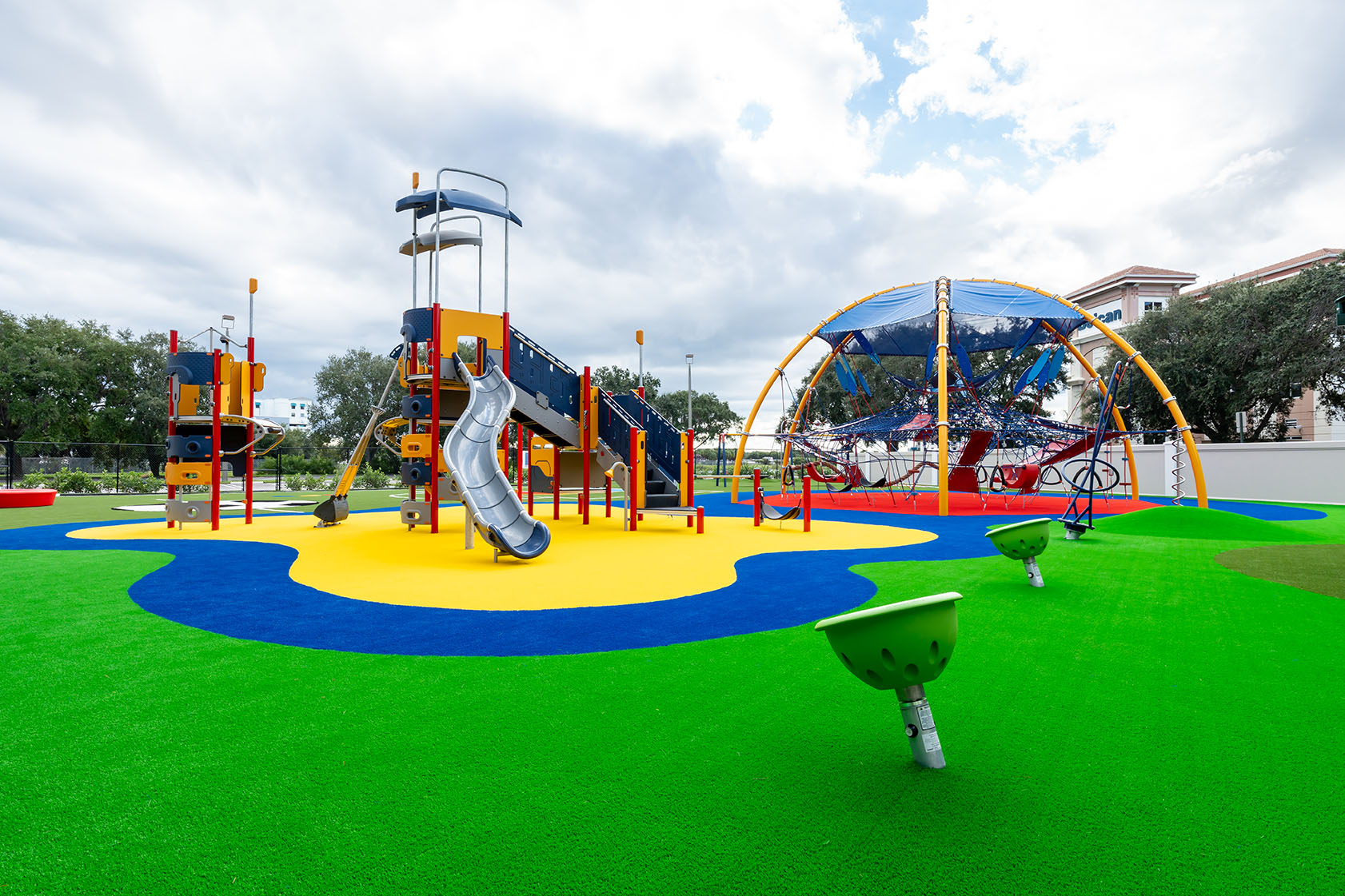 A wide shot of the playground at the Center for Creative Education in West Palm Beach, Florida, featuring custom poured-in-place surfacing, a large climbing dome, a play tower with a KOMPAN Cliff Rider, and various spinning elements