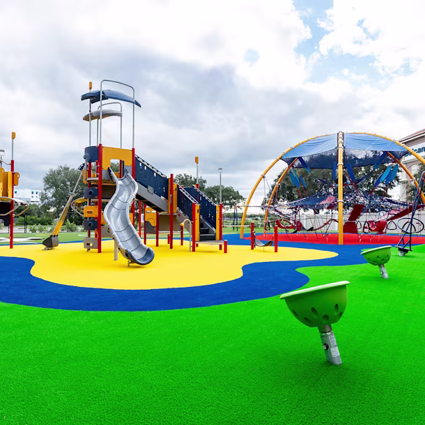 A wide shot of the playground at the Center for Creative Education in West Palm Beach, Florida, featuring custom poured-in-place surfacing, a large climbing dome, a play tower with a KOMPAN Cliff Rider, and various spinning elements