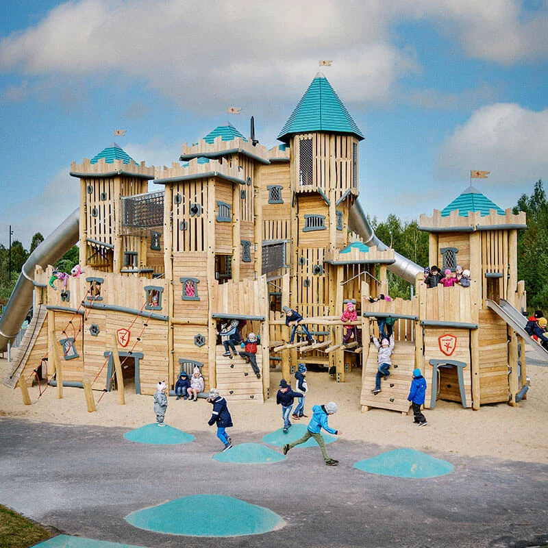 A group of children playing on a large scale natural wooden castle playground