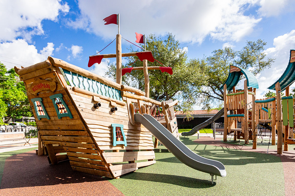 A wooden pirate ship with a slide and wooden play towers at Woodside Park in Miami, Florida