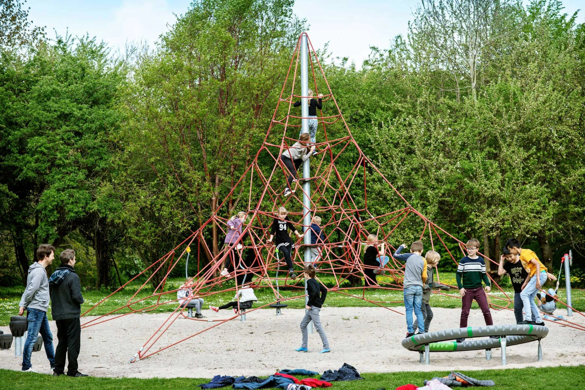En gruppe mennesker leger på en pyramideformet klatrestruktur på en legeplads.