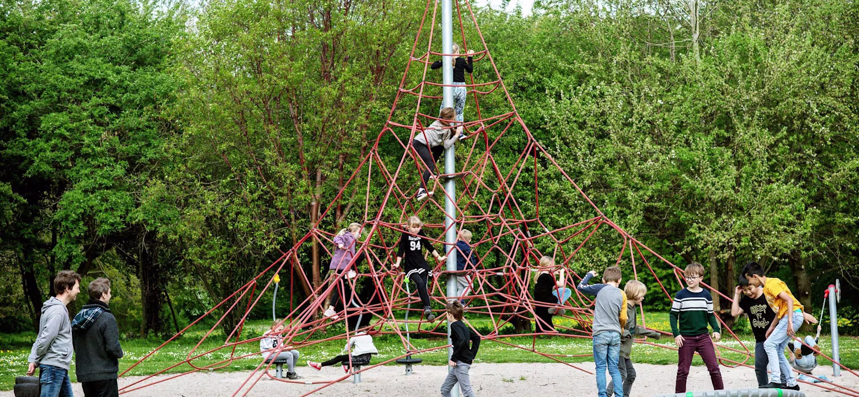 En gruppe mennesker leger på en pyramideformet klatrestruktur på en legeplads.