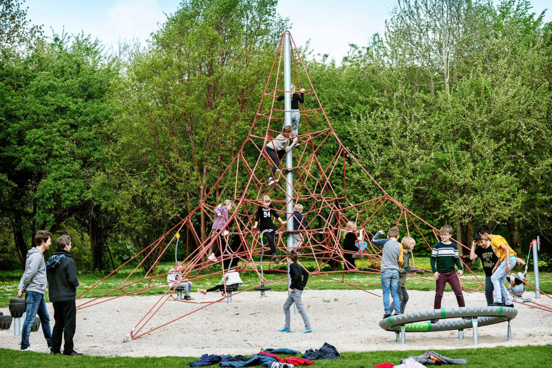 En gruppe mennesker leger på en pyramideformet klatrestruktur på en legeplads.