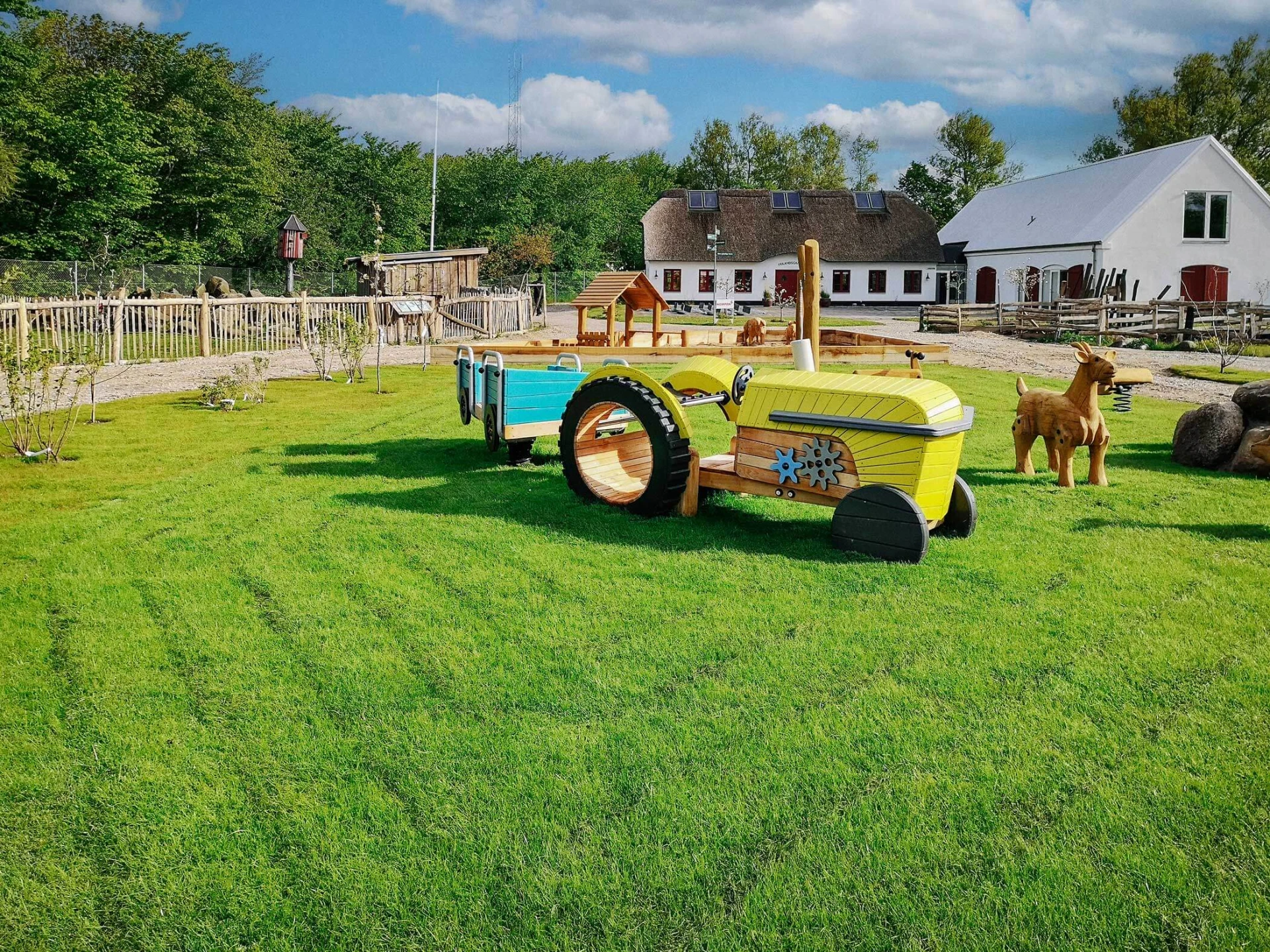 Pieni teemaleikkipaikka, jossa on puinen traktorileikkiväline ja puisia eläinveistoksia