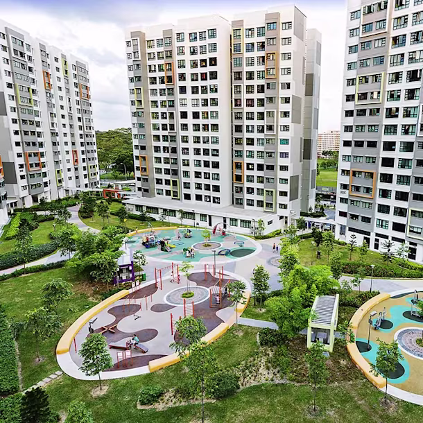 Tall apartment blocks overlook a colorful playground and paths in a landscaped green courtyard with trees and lawns