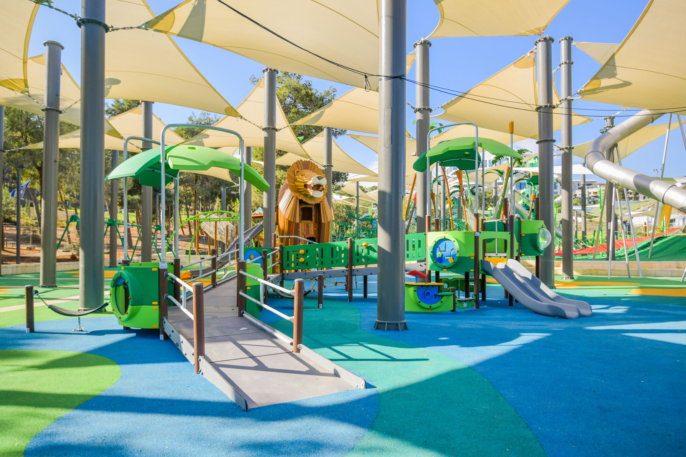 A girl in a striped outfit sliding down a yellow slide with bright blue surfacing underneath. Including bright colours within your playground construction details can produce vibrant and enticing results.