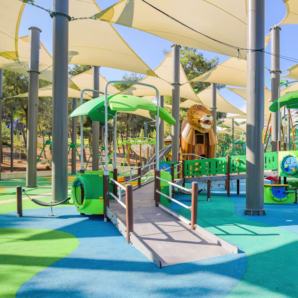 A girl in a striped outfit sliding down a yellow slide with bright blue surfacing underneath. Including bright colours within your playground construction details can produce vibrant and enticing results.