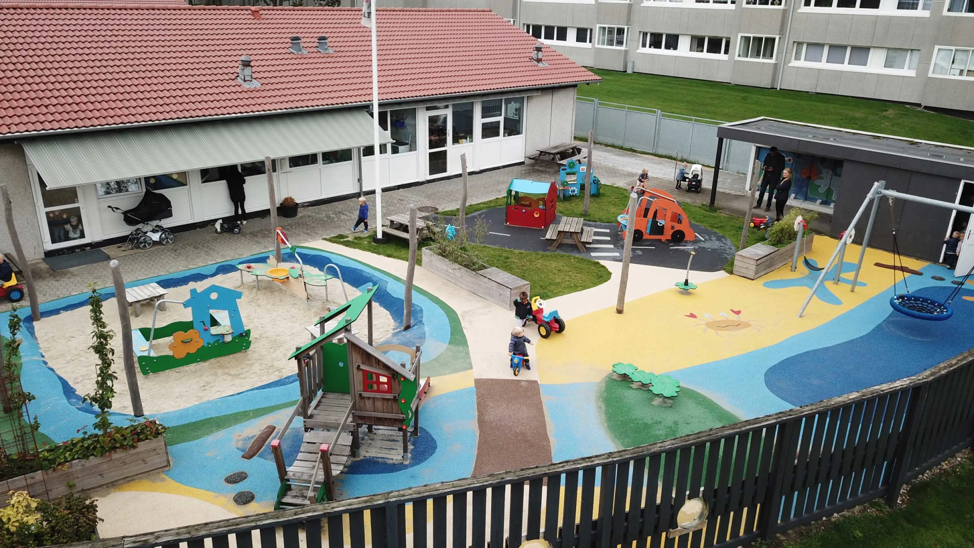 Drone photo of a colourful preschool playground with swings, wooden equipment, a sandpit and more. Offering different types of play is a great way to improve the popularity of your outdoor playground project.
