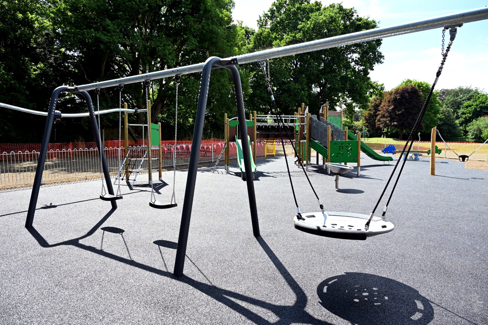 2 flat swings and a nest swing in front of a green and wooden children's playground unit