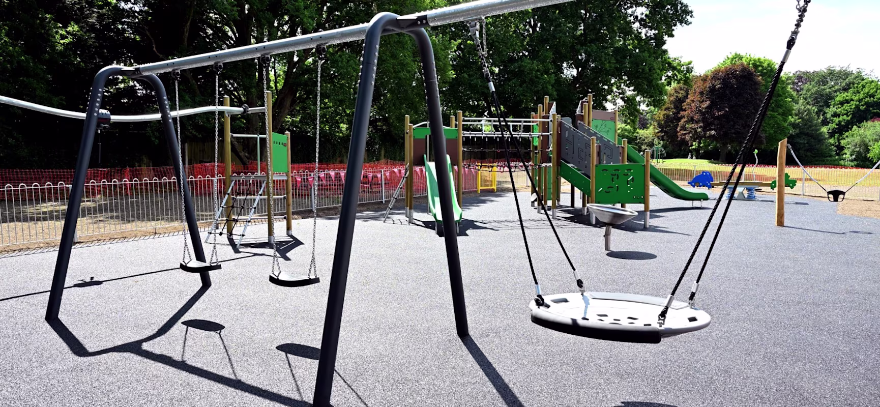 2 flat swings and a nest swing in front of a green and wooden children's playground unit